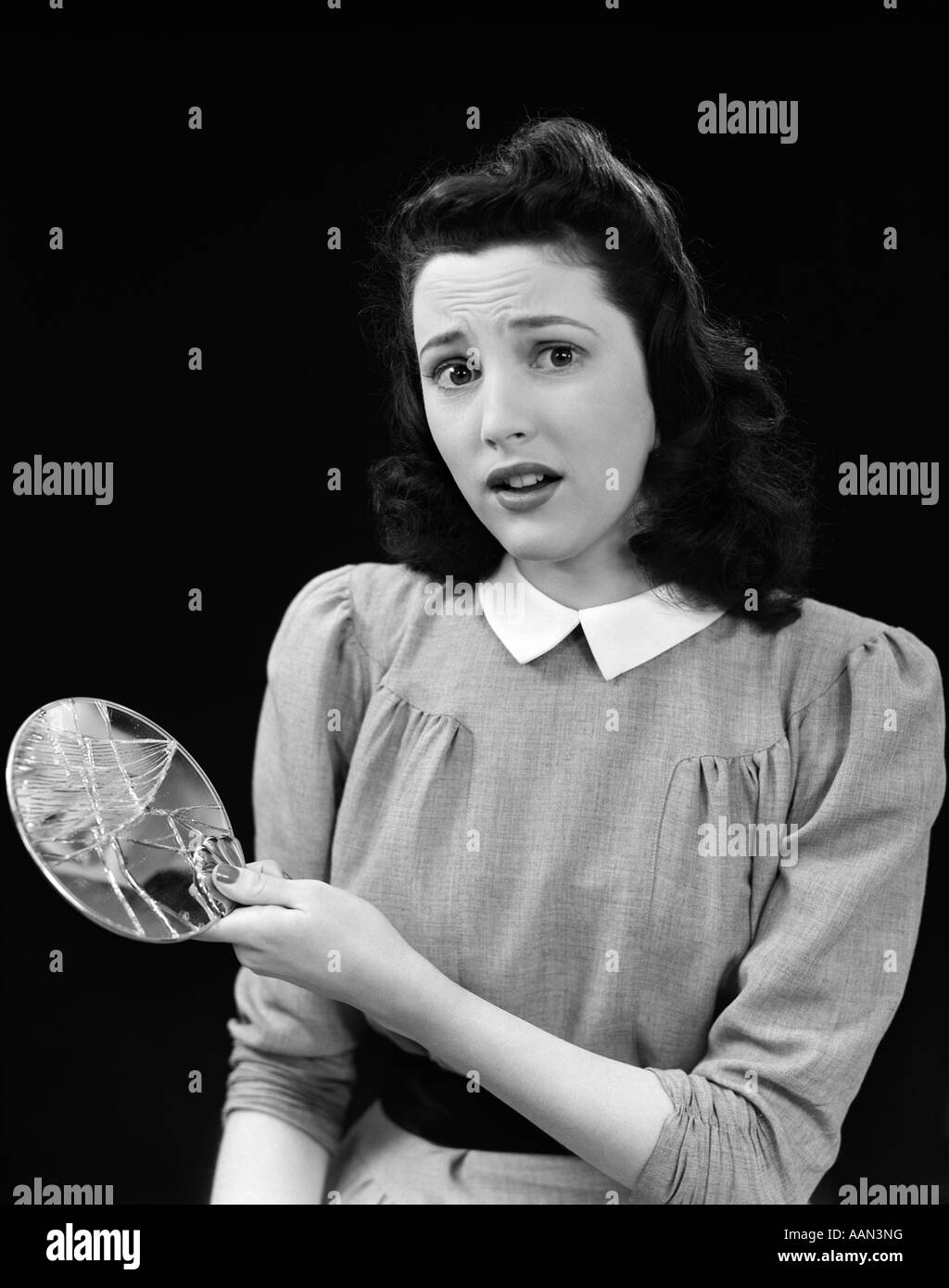 1940s donna azienda specchio rotto guardando la fotocamera con preoccupazione l'espressione del viso di sette anni di sfortuna Foto Stock