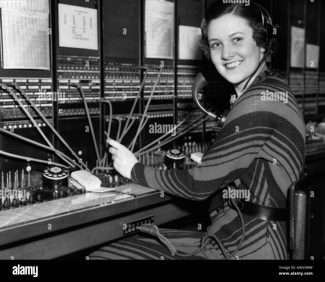 1930s donna OPERATORE TELEFONICO A SWITCHBOARD GUARDANDO sorridente della fotocamera Foto Stock