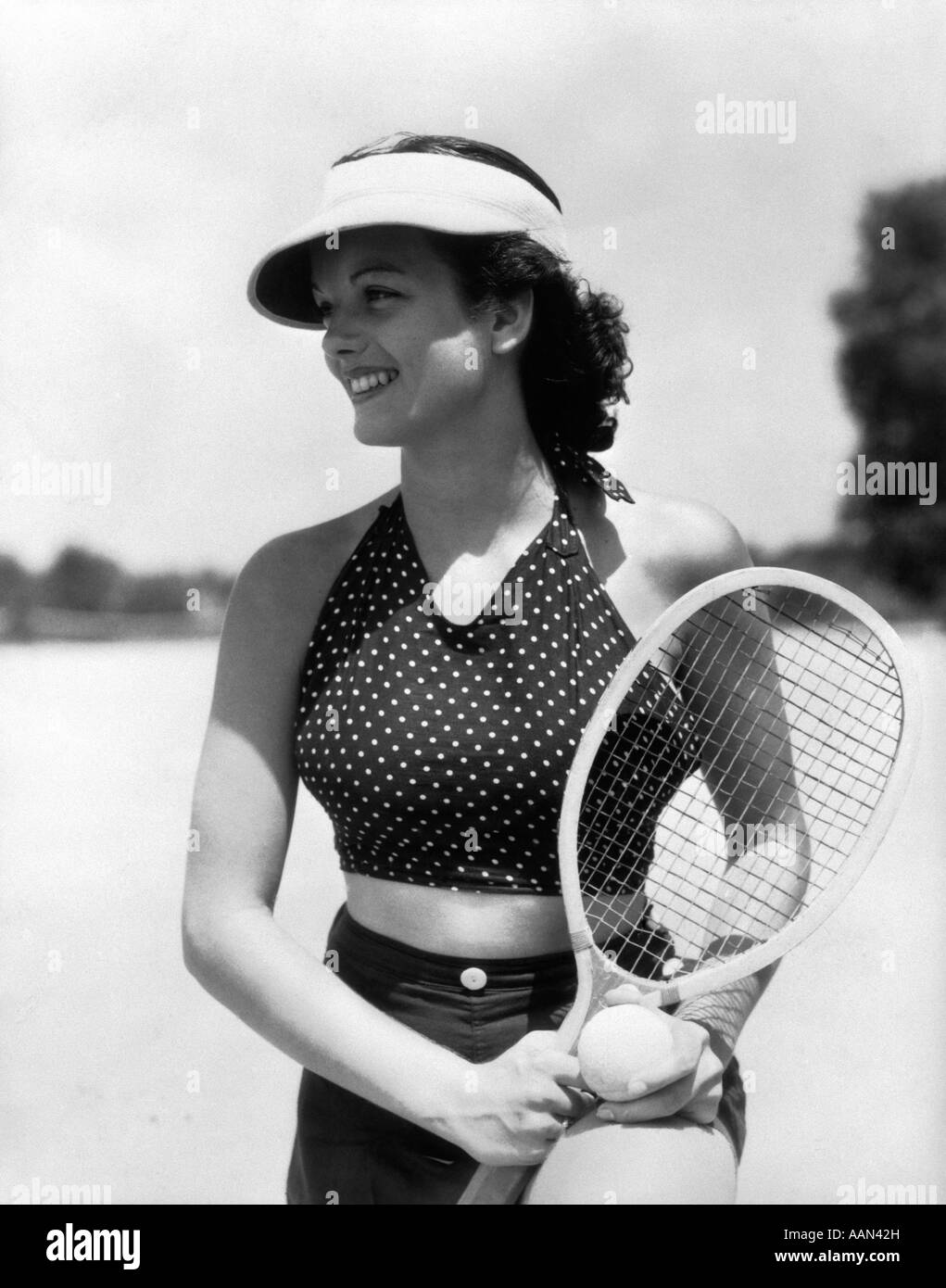 1930s DONNA IN POLKA DOT HALTER TOP SHORTS & VISIERA PARASOLE in possesso di una palla da tennis e delle racchette Foto Stock