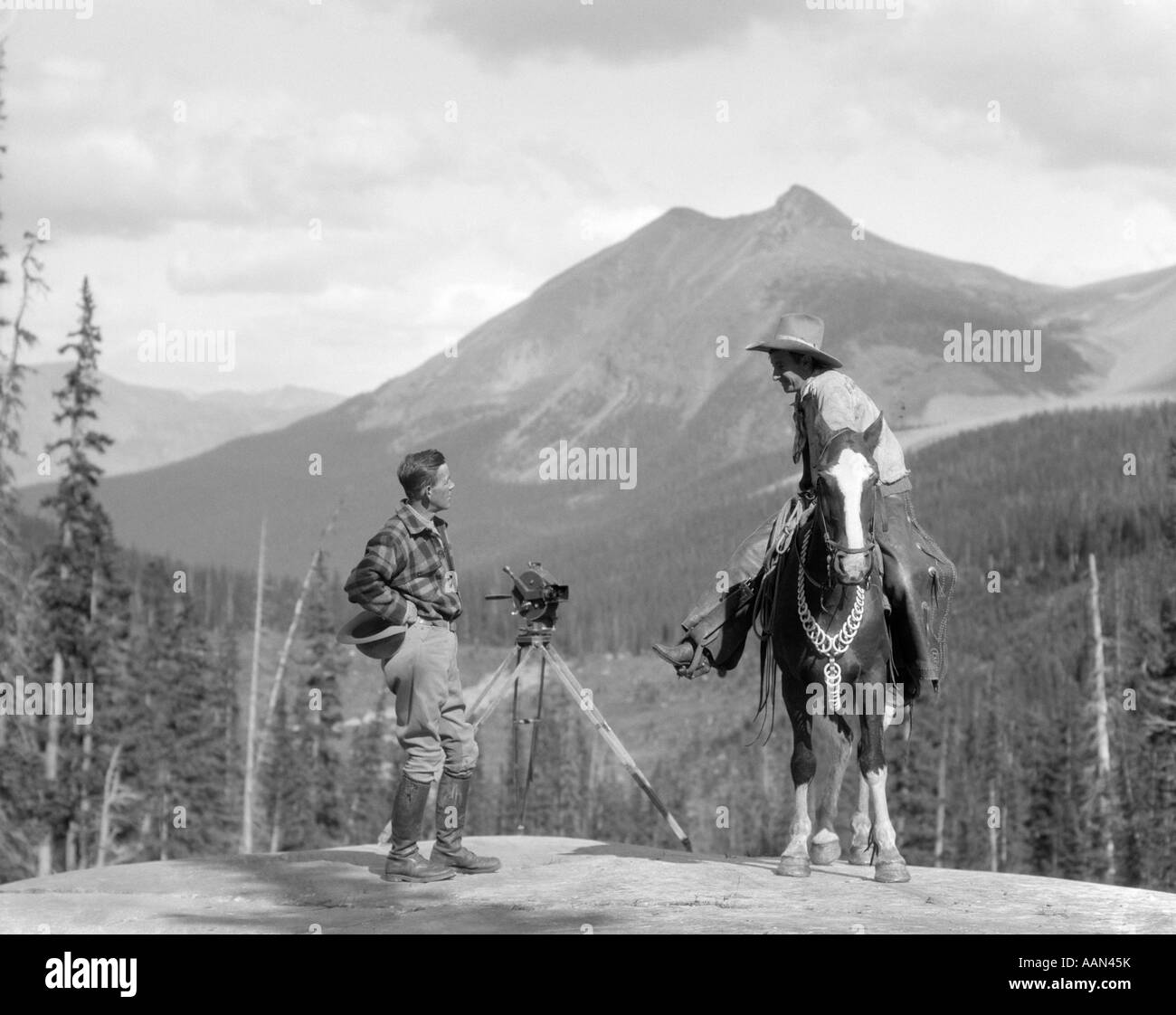 1930s cameraman in stivali i jodhpurs & lana maglietta di caccia in piedi accanto alla macchina fotografica del film su un cavalletto a parlare con montato il COWBOY Foto Stock