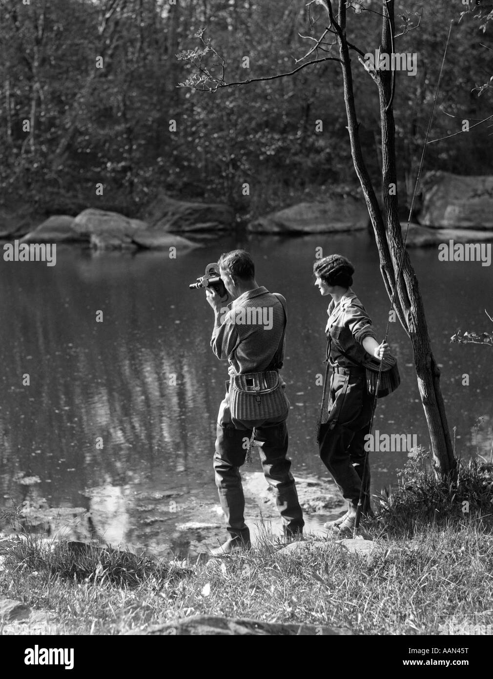1930 L'uomo con la macchina fotografica del film & donna con la trota canna da pesca sono entrambi indossando WADERS & nasse di vimini Foto Stock