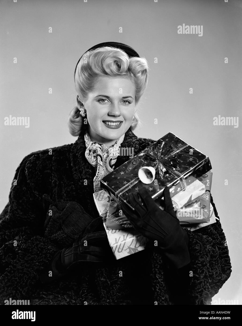 1940s giovane donna bionda che indossa il persiano agnello guanti di rivestimento portante avvolto regali di Natale guardando la fotocamera Foto Stock