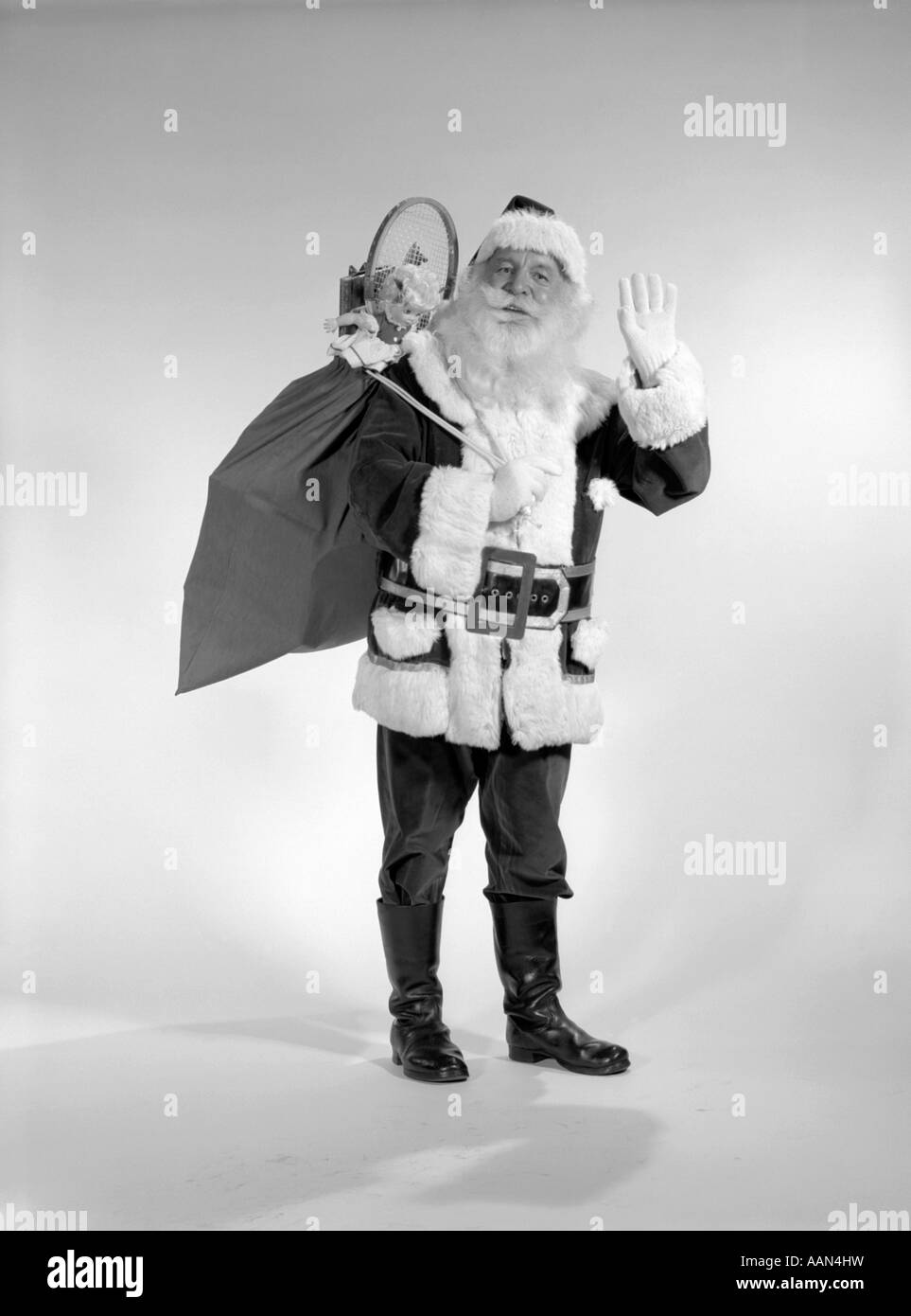 Anni sessanta sorridente SANTA CON UN SACCO DI GIOCATTOLI sulla sua schiena sventolando JOLLY Foto Stock