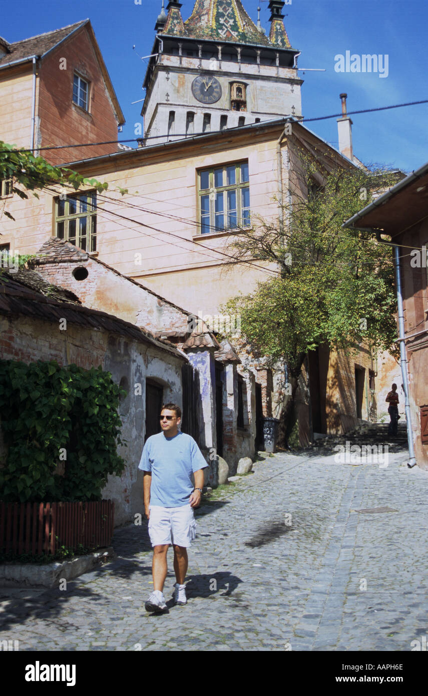 Un turista passeggiate attraverso medievale di Sighisoara in Transilvania meridionale medievale torre orologio sul lato posteriore Foto Stock
