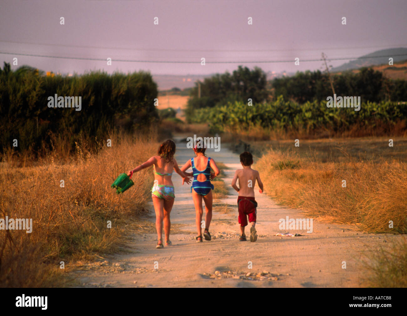 Tre bambini in nuotatori a piedi lungo un sentiero polveroso dopo una giornata in spiaggia Foto Stock