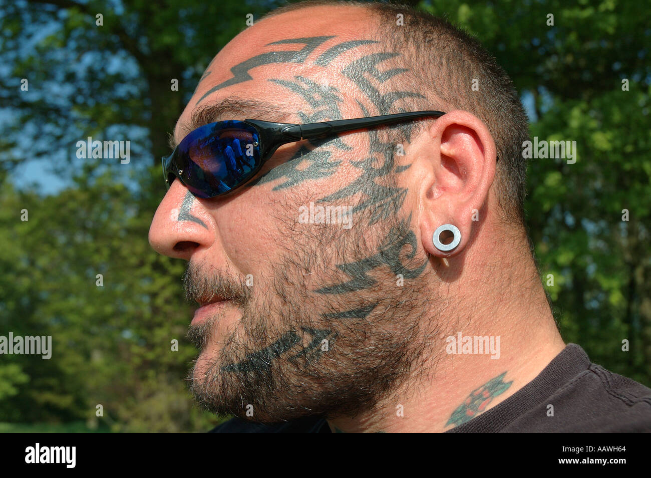 Ritratto di Uomo con occhiali scuri e tatuaggi sul viso e braccia e  piercing Foto stock - Alamy