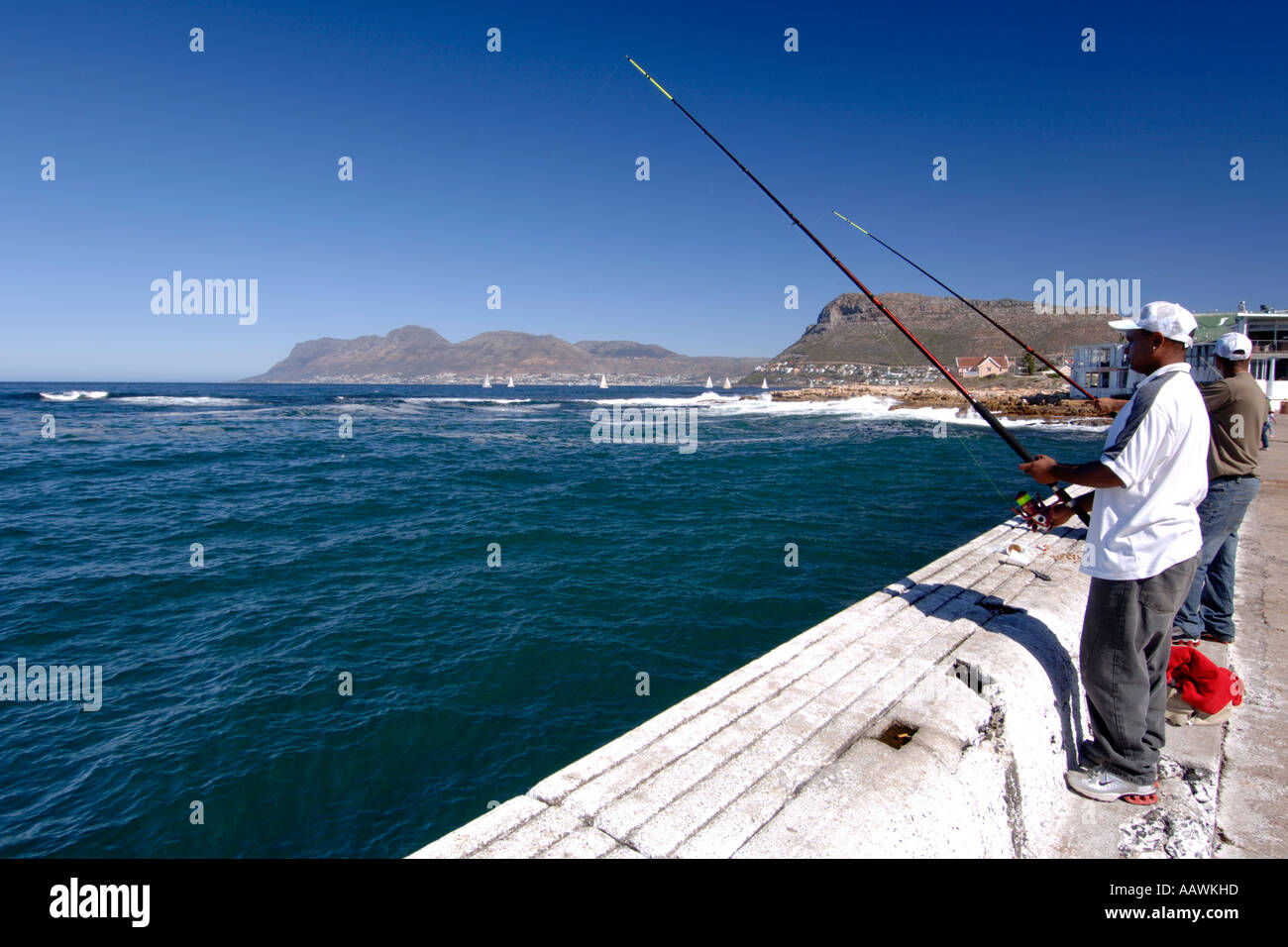 Uomini di colore pesca dal molo di Kalk Bay Harbor in Cape Town, Sud Africa. Foto Stock