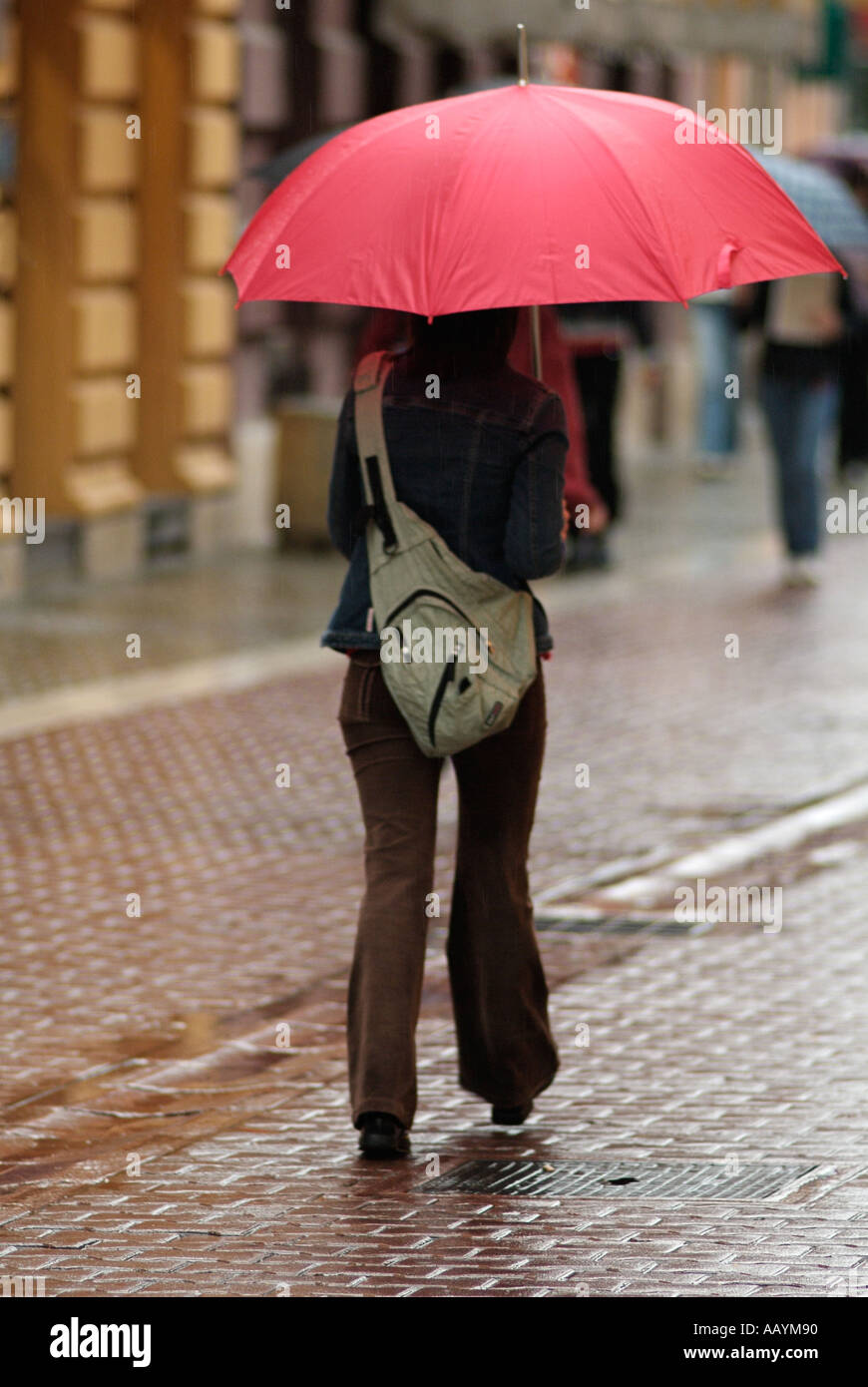 Giovane donna con un ombrello rosso in una strada trafficata in un giorno di pioggia Foto Stock