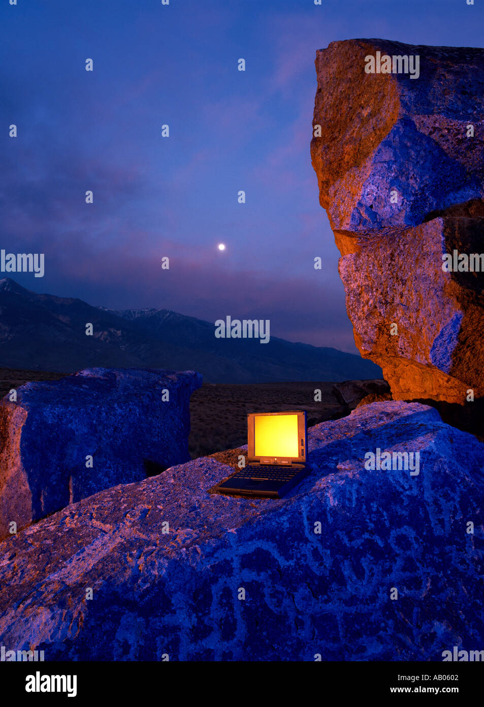 La luna sorge nel cielo dietro un computer portatile con schermo giallo situato proprio in cima a una roccia con incisioni rupestri vicino al Vescovo California Foto Stock