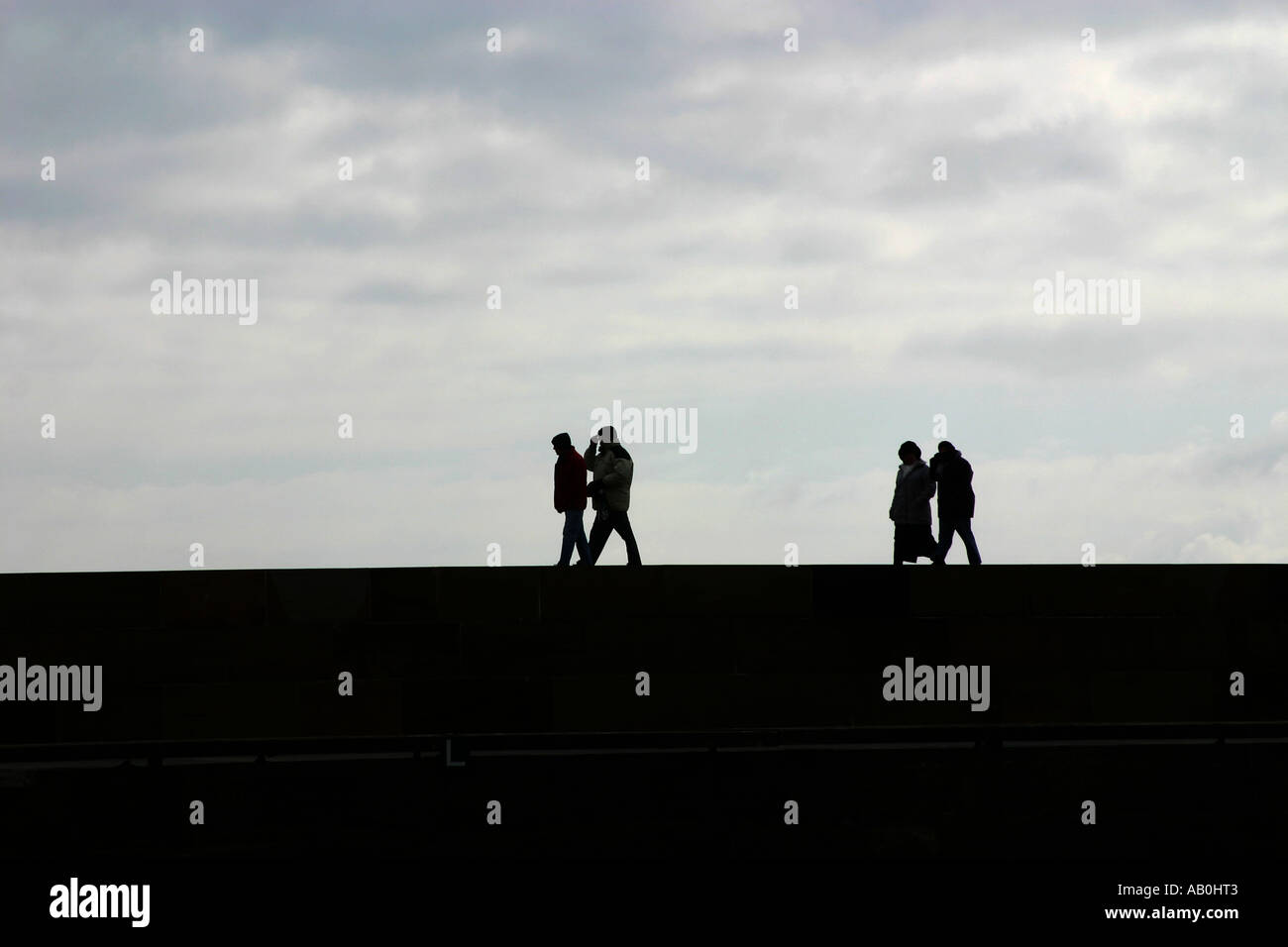 Quattro persone a piedi lungo la parte superiore di una parete del porto in silhouette. Foto Stock