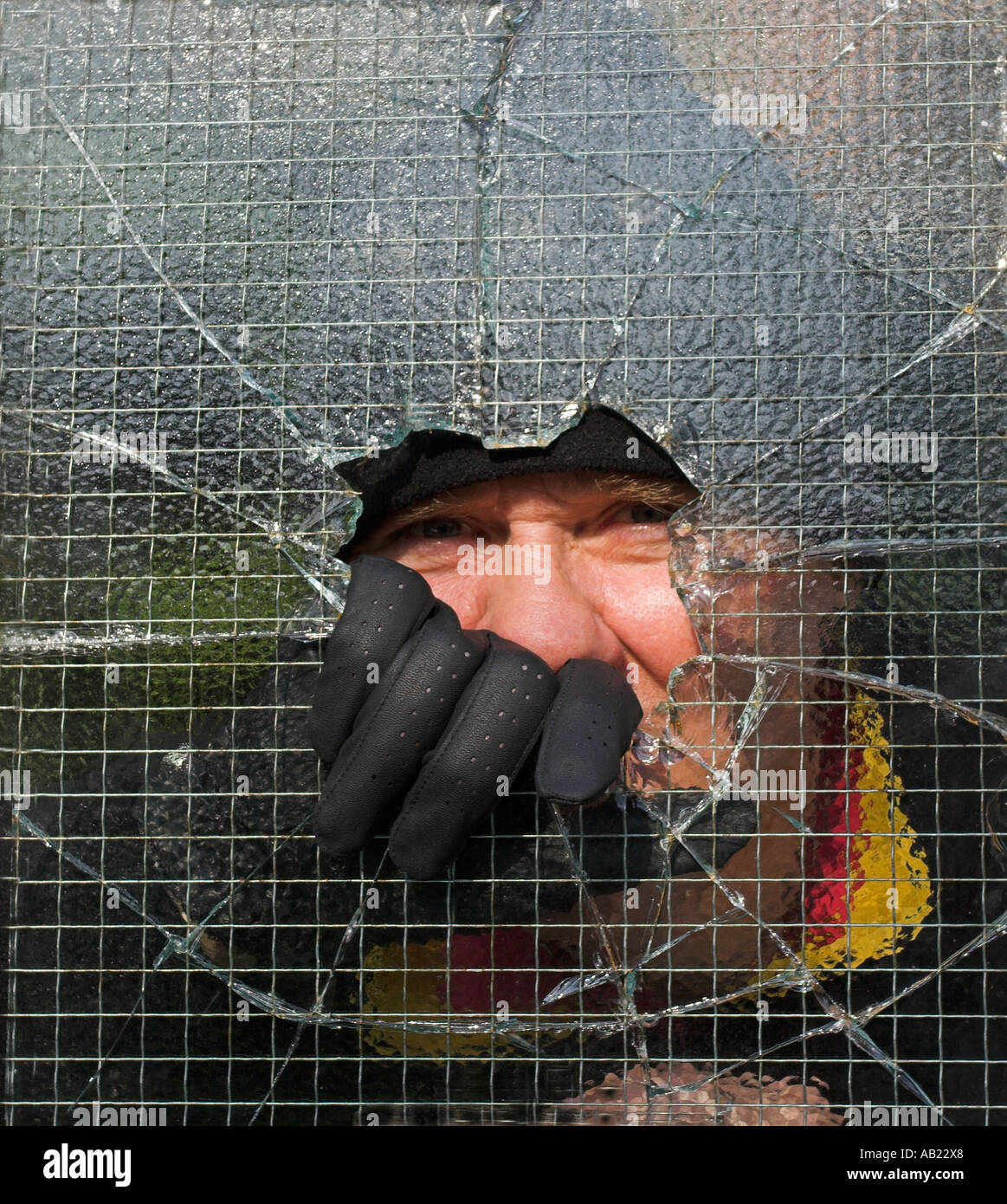 Ladro di rottura e di entrare in una proprietà privata da smashing attraverso il filo metallico applicato vetro. Foto Stock