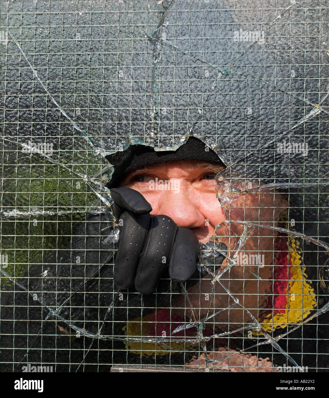 Ladro di rottura e di entrare in una proprietà privata da smashing attraverso il filo metallico applicato vetro. Foto Stock