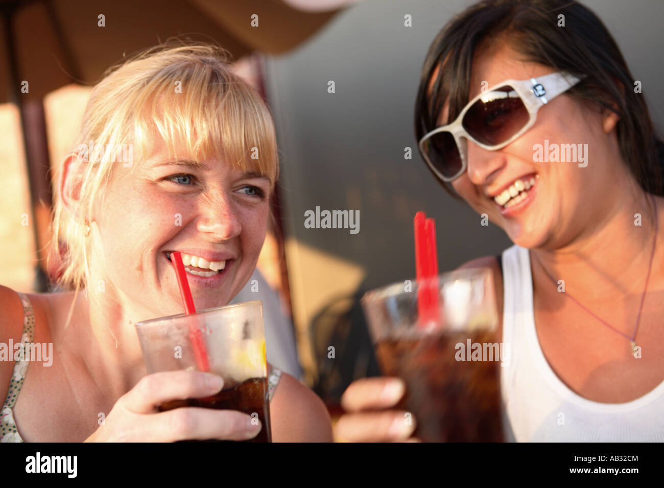 Due donne seduti all'aperto con bevande a ridere Foto Stock