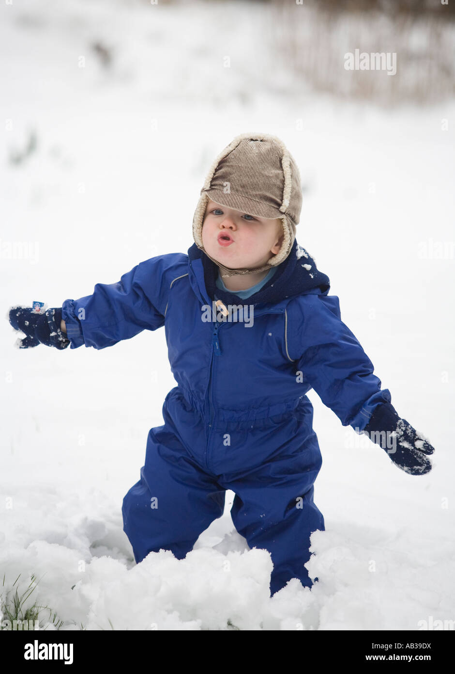 Un giovane ragazzo di età compresa tra i diciotto mesi in un impermeabile blu gioca nella neve Foto Stock