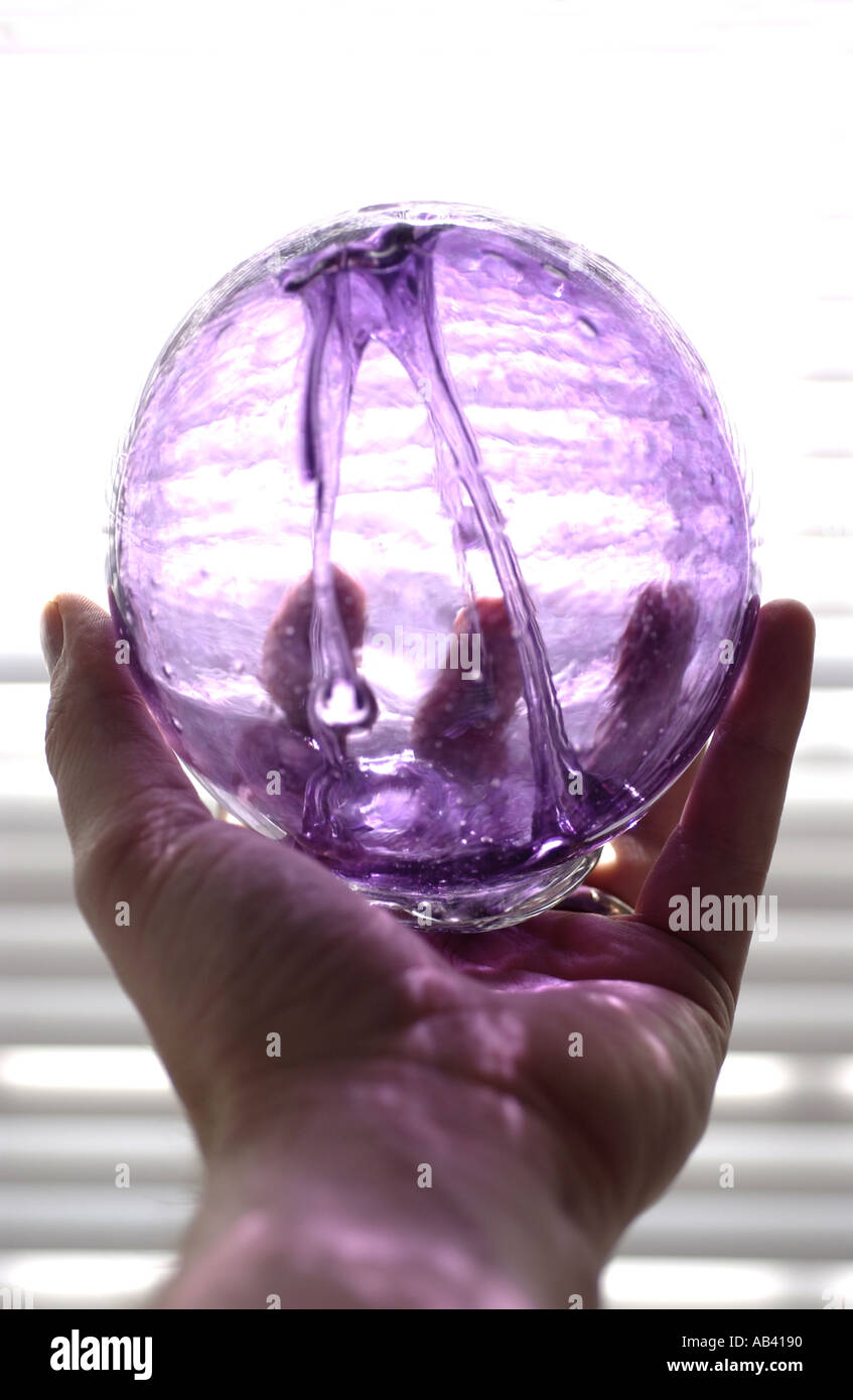 Mano che tiene un viola globo di vetro vicino alla lampada Foto Stock