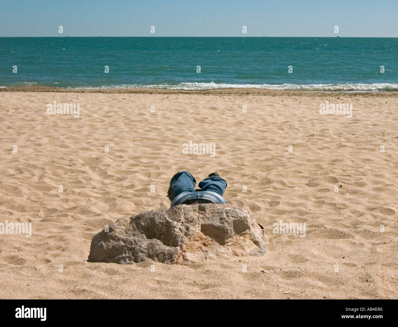 Lone sunbather in jeans addormentato dietro la roccia sulla spiaggia di Palavas les flots Foto Stock