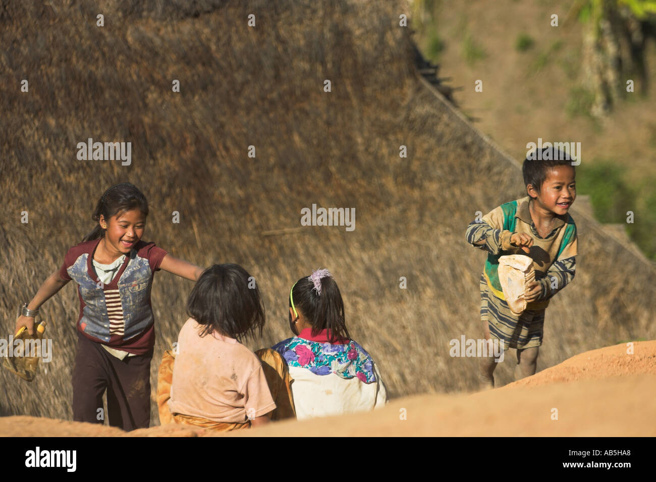 Myanmar stato Shan Ann villaggio nei pressi di Kengtung Ann i bambini lo scorrimento verso il basso della pendenza di fango al di fuori di casa di paglia Foto Stock