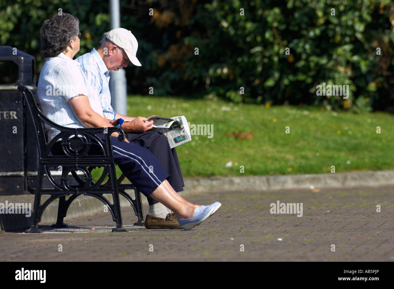Anziano uomo e donna giovane leggendo un giornale su una panchina del parco a sunshine warrenpoint Irlanda del Nord Foto Stock
