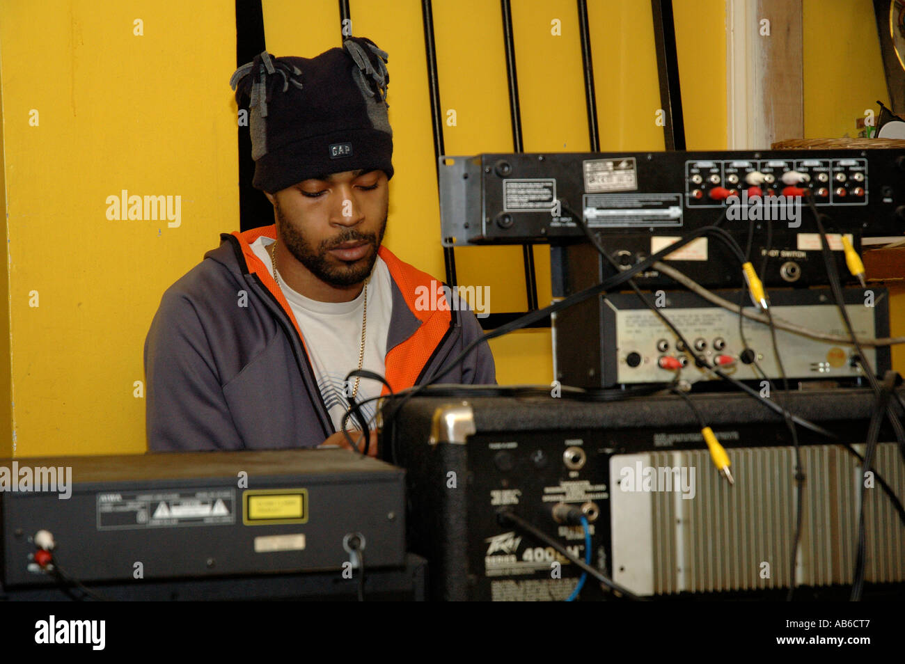 Giovane musicista mixare brani mentre artisti rap esegue a Rastafarian comunità casa nel sud di Londra. Foto Stock