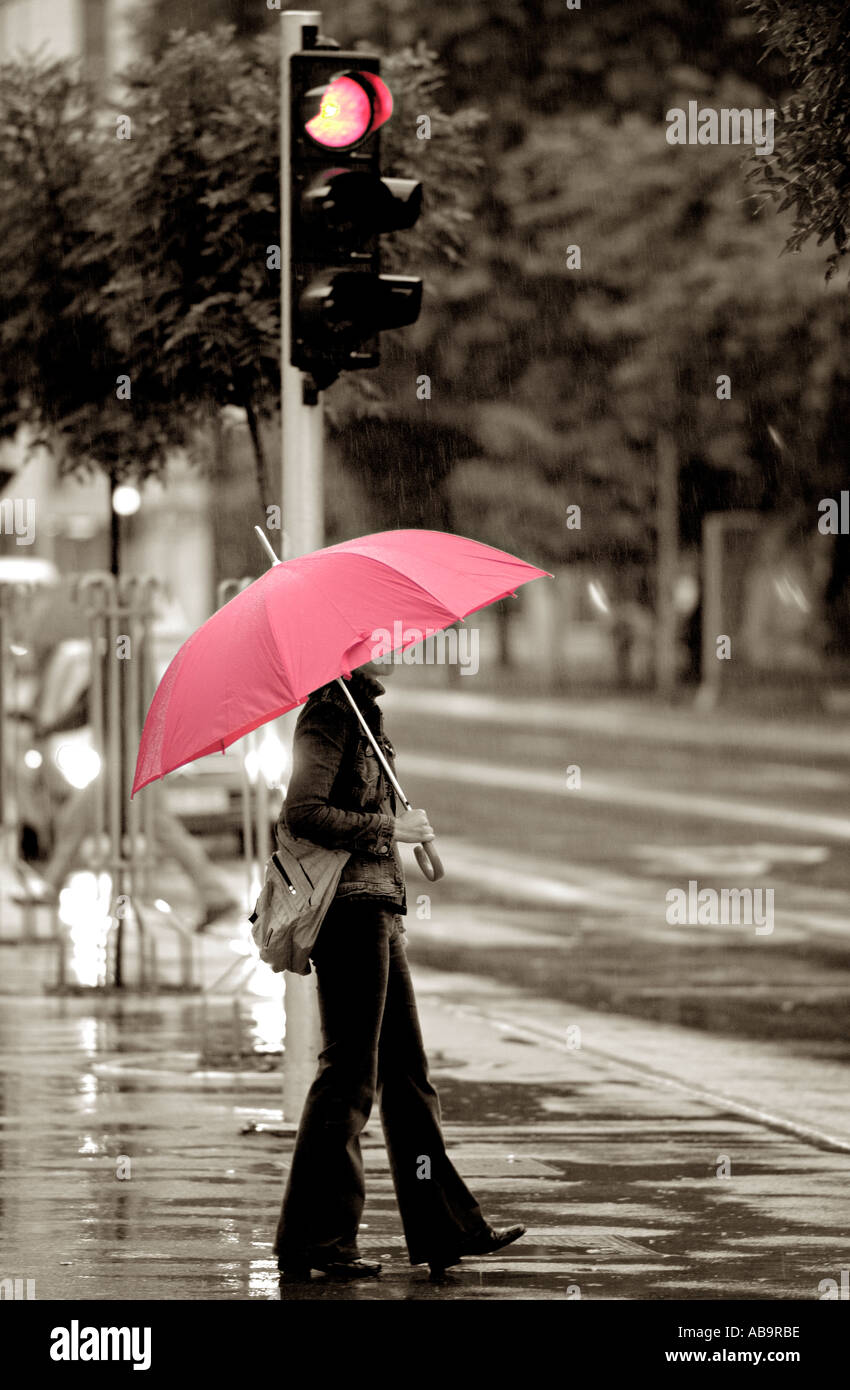 Donna con ombrello rosso su una strada di città in un giorno di pioggia Foto Stock