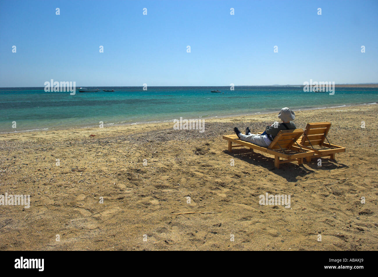 Reclinabile in legno sedie a sdraio sulla spiaggia Tondoba Mar Rosso in Egitto con la donna nel cappello per il sole e abbigliamento protettivo Foto Stock