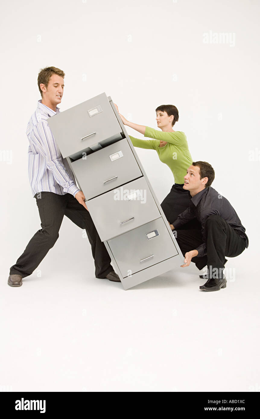 Tre lavoratori ufficio il sollevamento di un carico pesante Filing cabinet Foto Stock