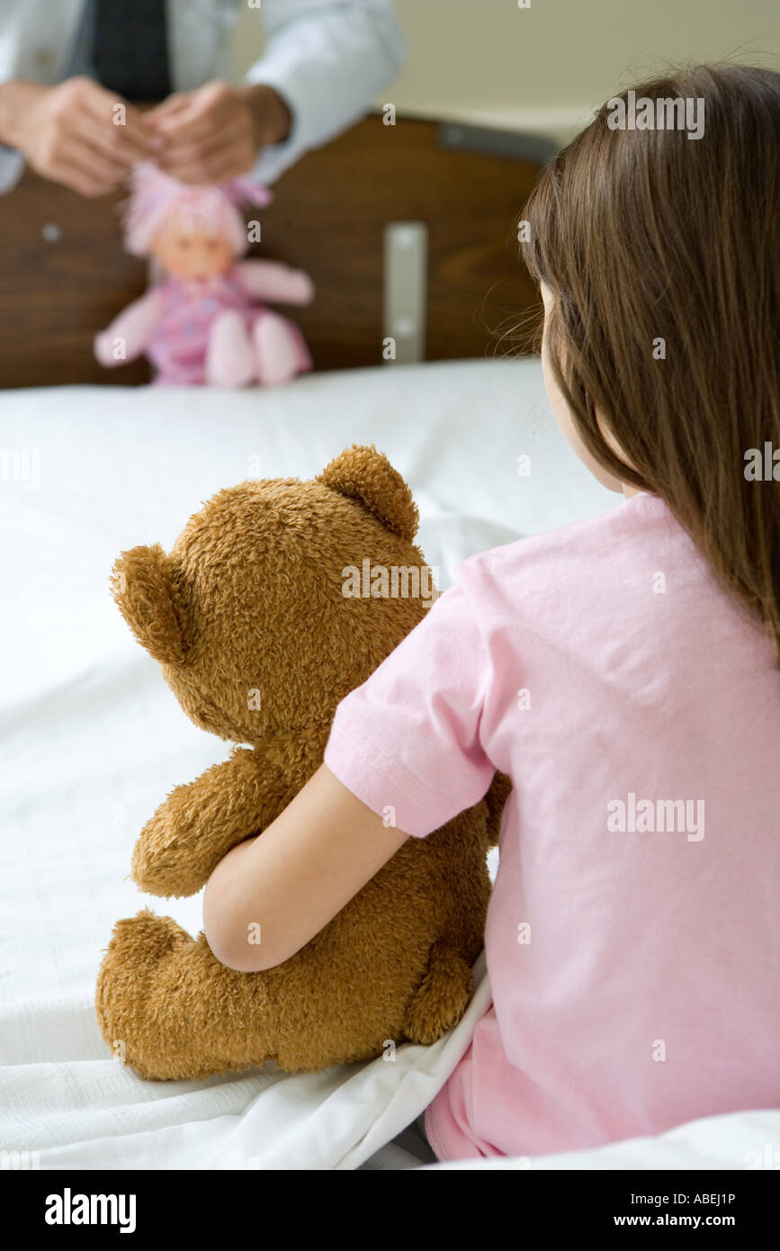 Ragazza seduta nel letto di ospedale holding Teddy bear, di fronte medico tenendo la bambola Foto Stock