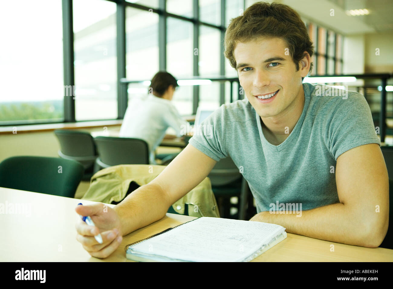 Collegio maschile studente seduto a tavola, sorridente in telecamera Foto Stock