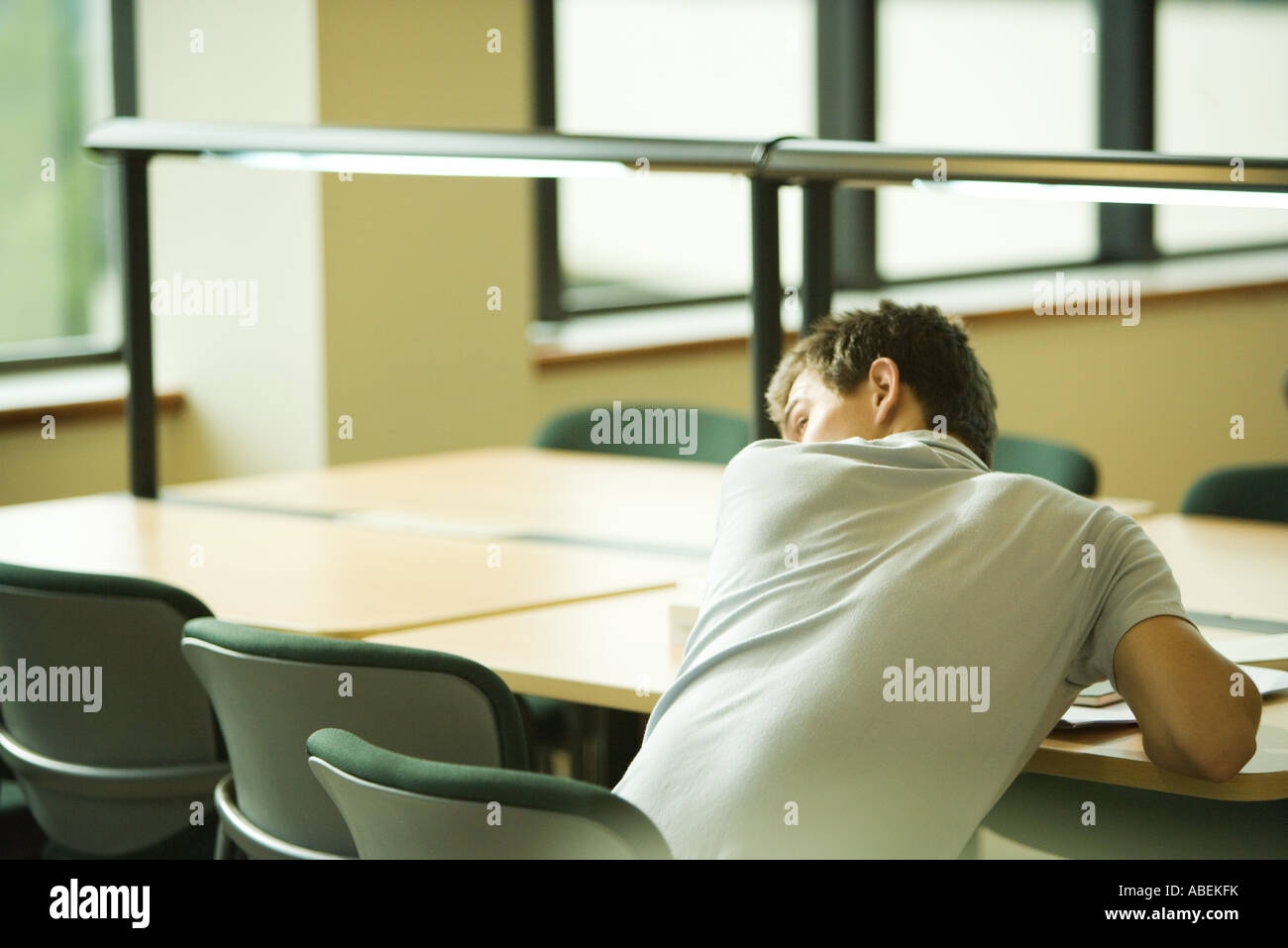 Collegio maschile studente seduto a tavola, guardando sopra la spalla Foto Stock