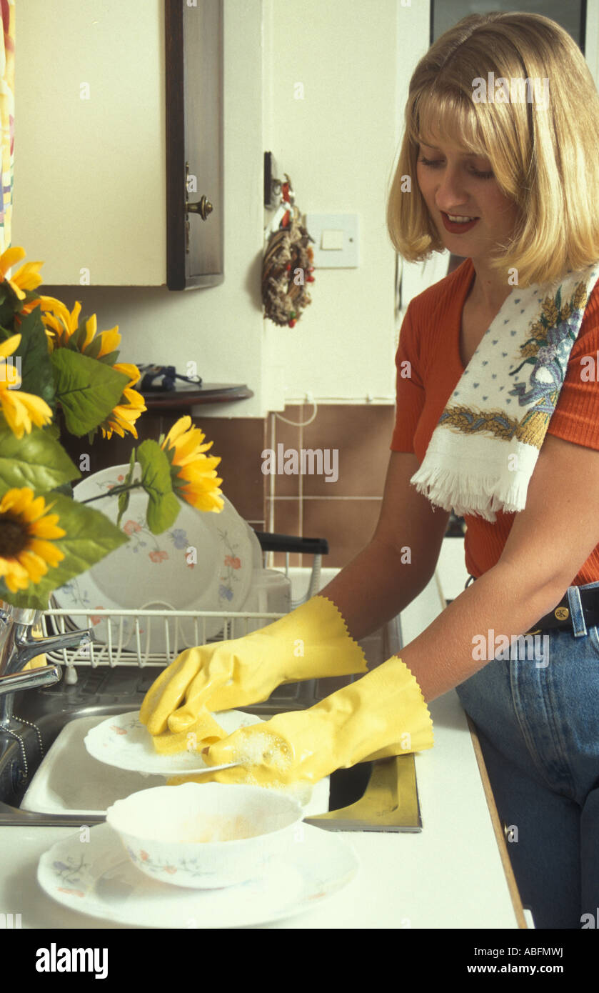 Giovane donna bionda lavaggio piatti al lavello da cucina Foto Stock