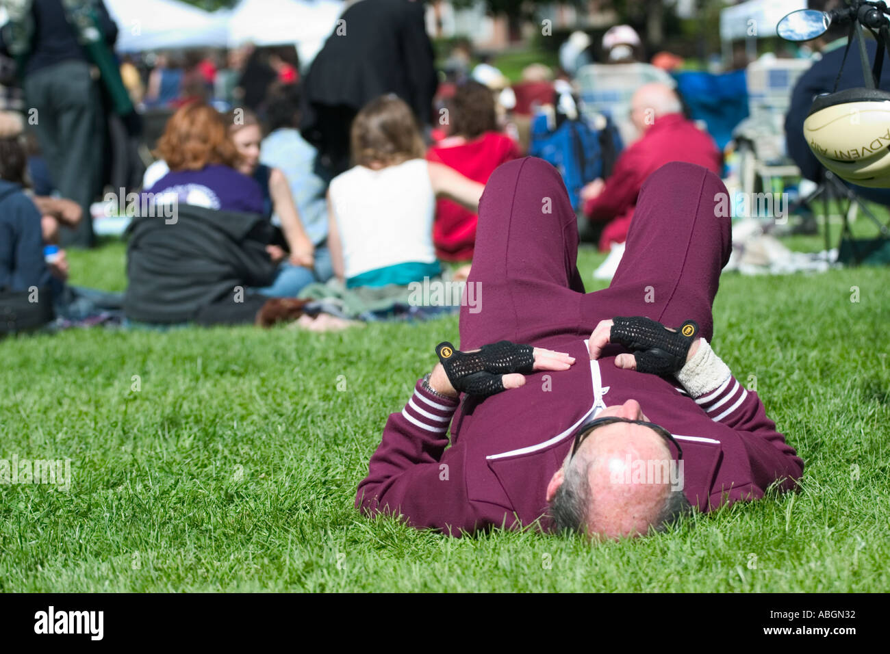 La mezza età balding uomo che indossa una tuta da jogging sdraiati sull'erba vicino a una folla ad un concerto Foto Stock