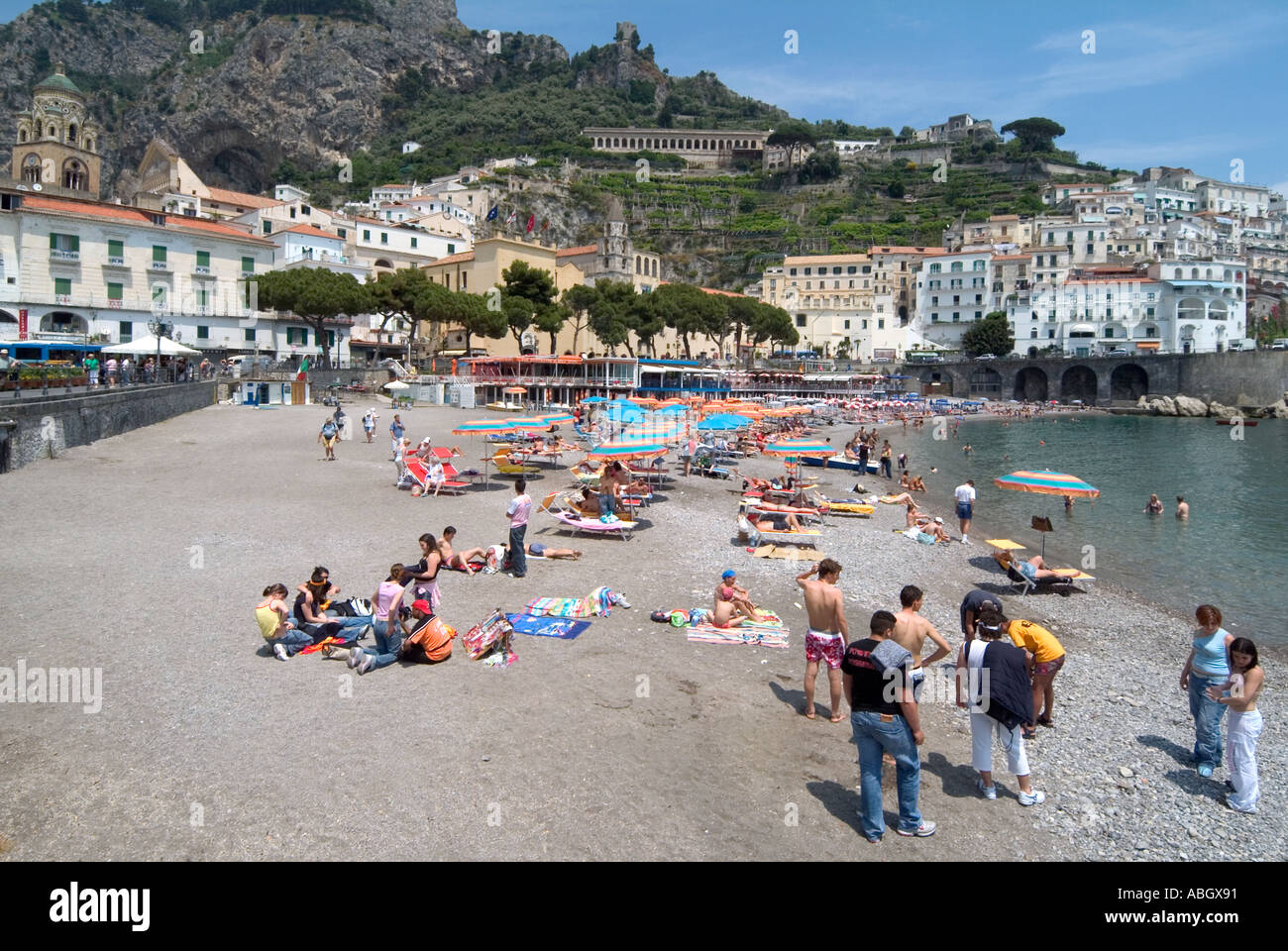 Gruppi di turisti e abitanti del luogo sulla spiaggia di Amalfi, vista sul mare, ombrelloni e paesaggio collinare, Campania Salerno Italia e UE Foto Stock