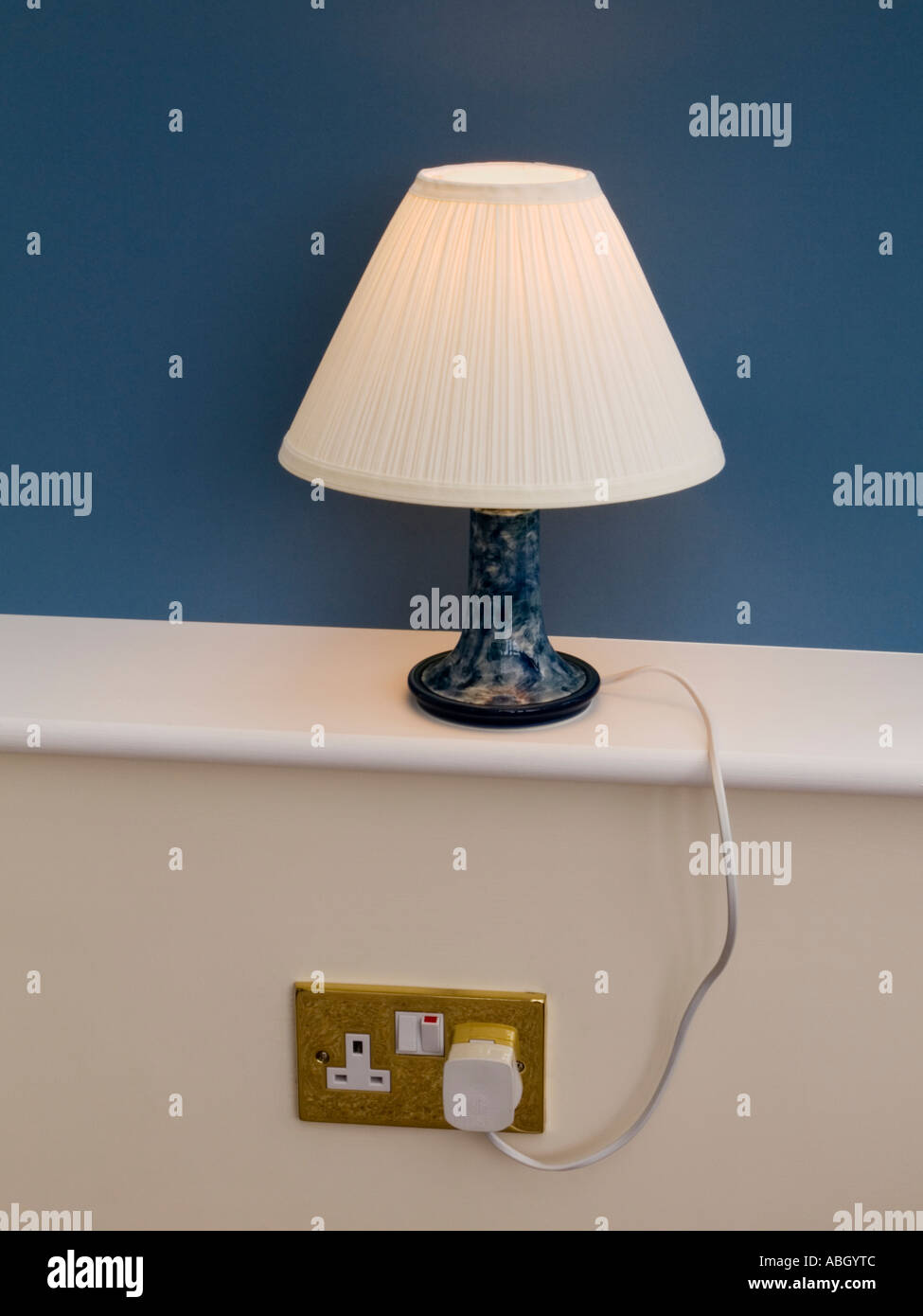 Lampada da tavolo illuminato paralume bianco sul davanzale con blue dietro inserito nella presa di corrente a muro che mostra il cavo. Inghilterra Regno Unito Gran Bretagna Foto Stock