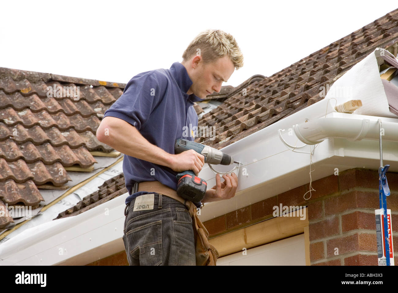 Un costruttore di installazione delle staffe per tenere una gronda al di sotto di un tetto di una casa. Foto Stock