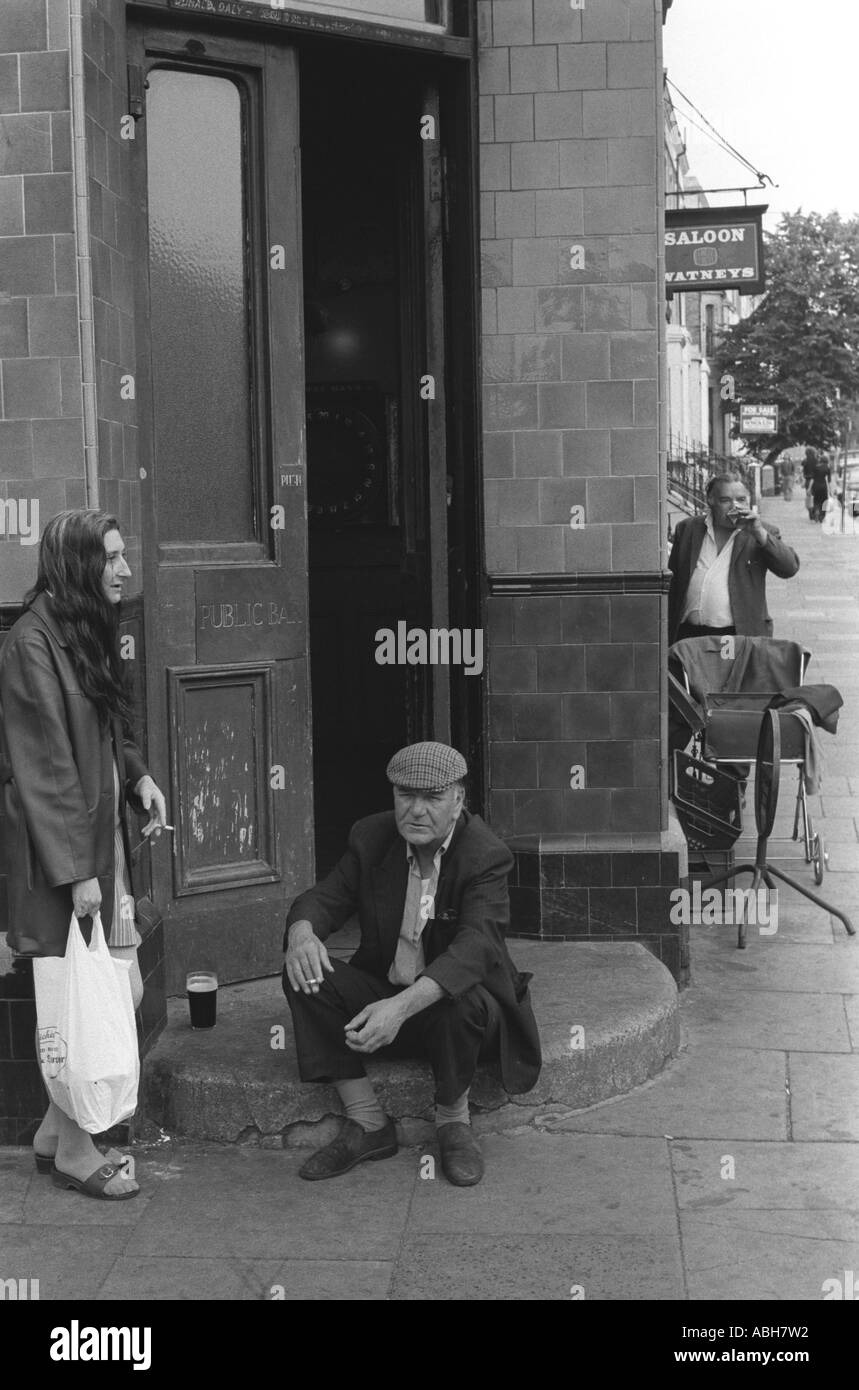 Classe operaia coppia 1970s Regno Unito. Coppia che beve e fuma seduti sul gradino di un pub Watneys Saloon. Notting Hill Londra Inghilterra. 1975 HOMER SYKES Foto Stock
