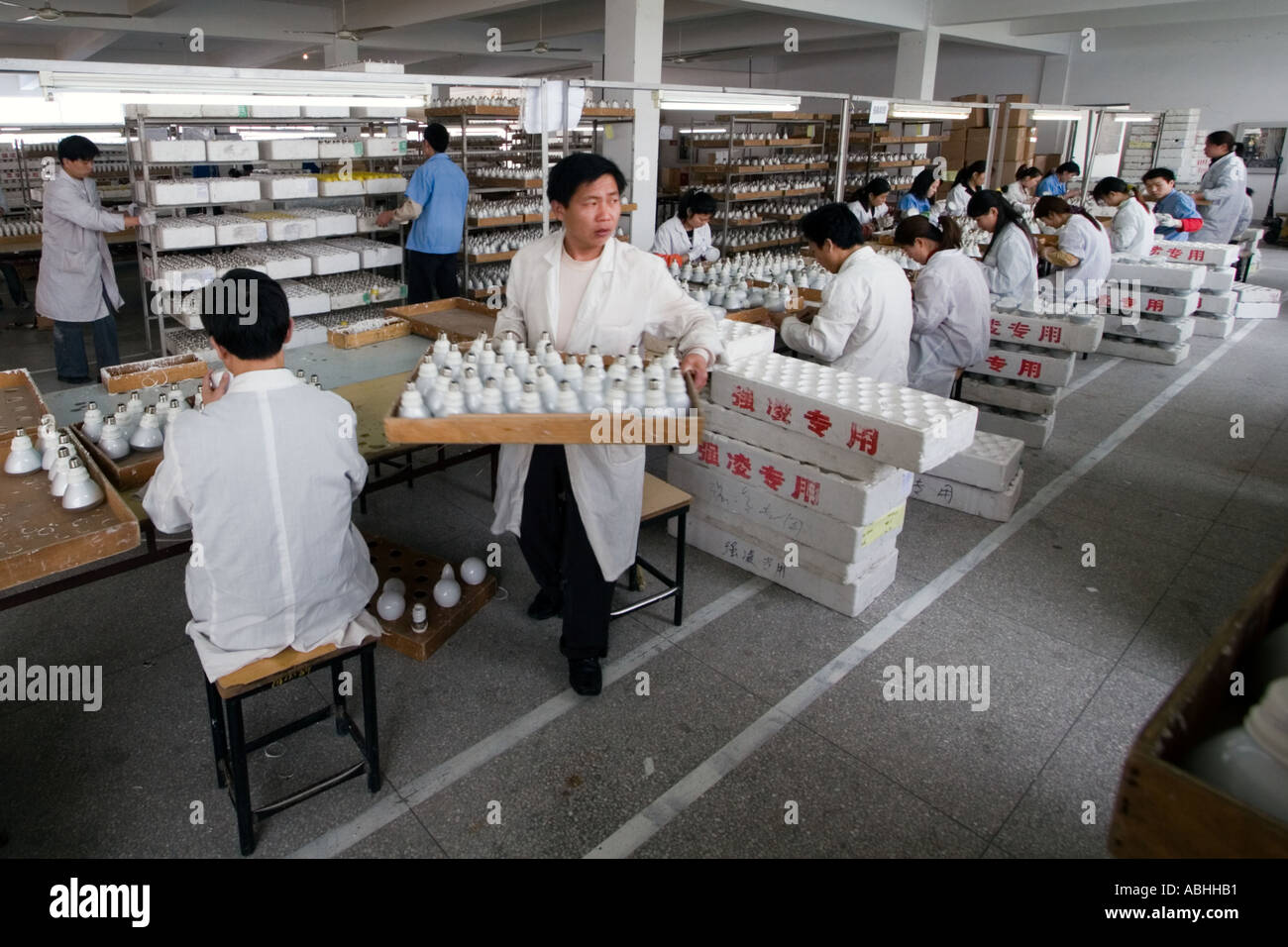 Un operaio di fabbrica si muove finito di illuminazione prodotti dalla sua postazione a Shanghai in Cina Foto Stock