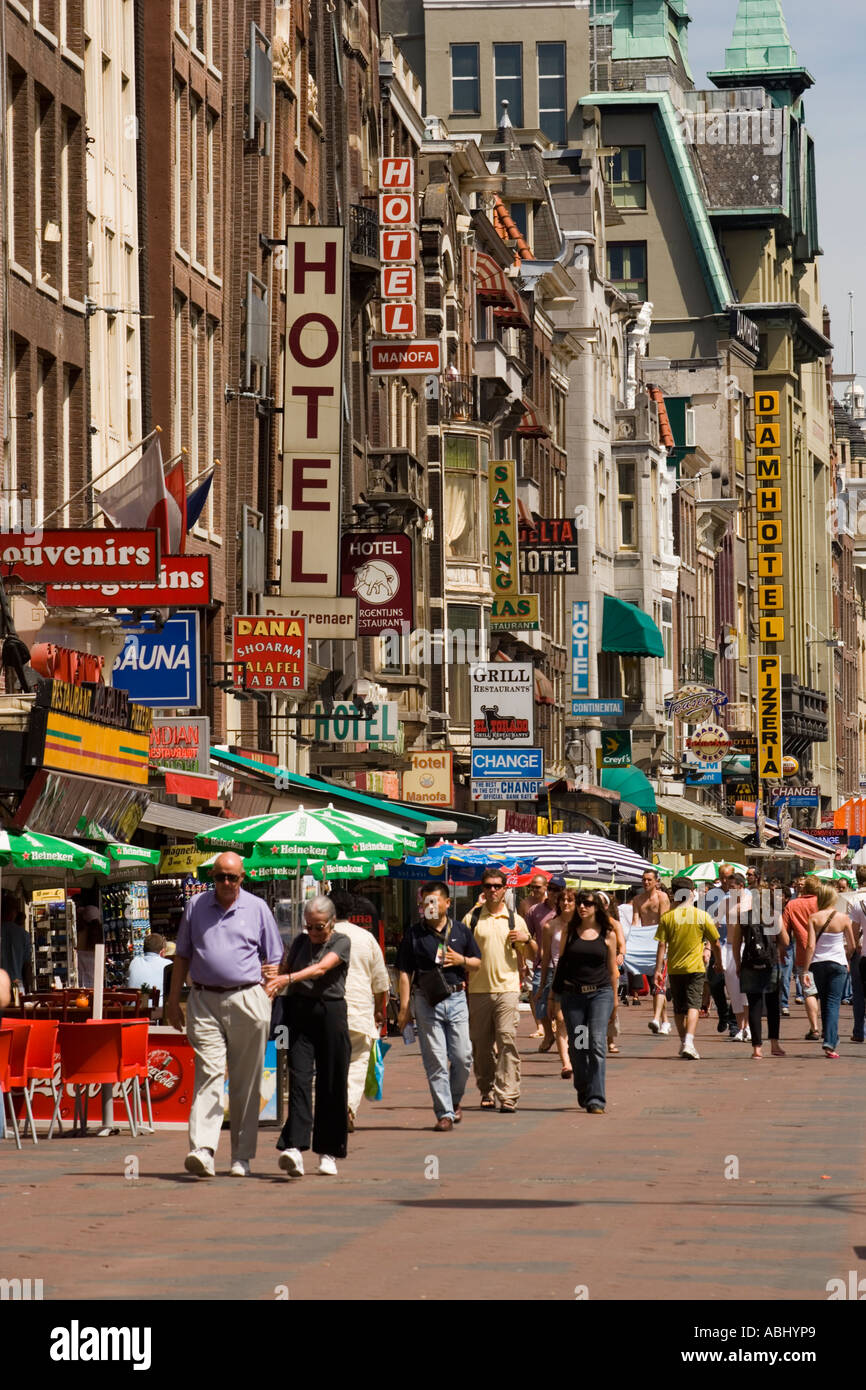 La gente camminare sulla strada dello shopping con un sacco di negozi di souvenir Damrak Amsterdam Olanda Paesi Bassi Foto Stock