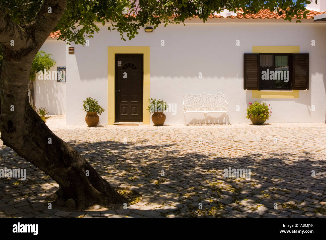 Un bianco villa fortificata in Algarve, fronteggiata da un ombreggiato cortile in ciottoli Foto Stock