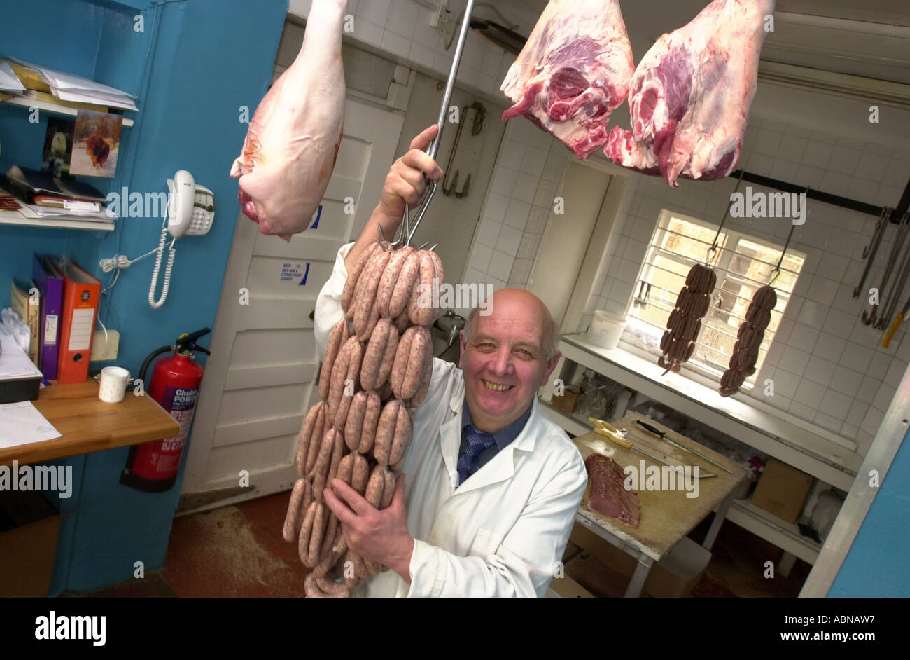 Butcher contiene una stringa di salsicce appeso ad un gancio nel suo negozio REGNO UNITO Foto Stock