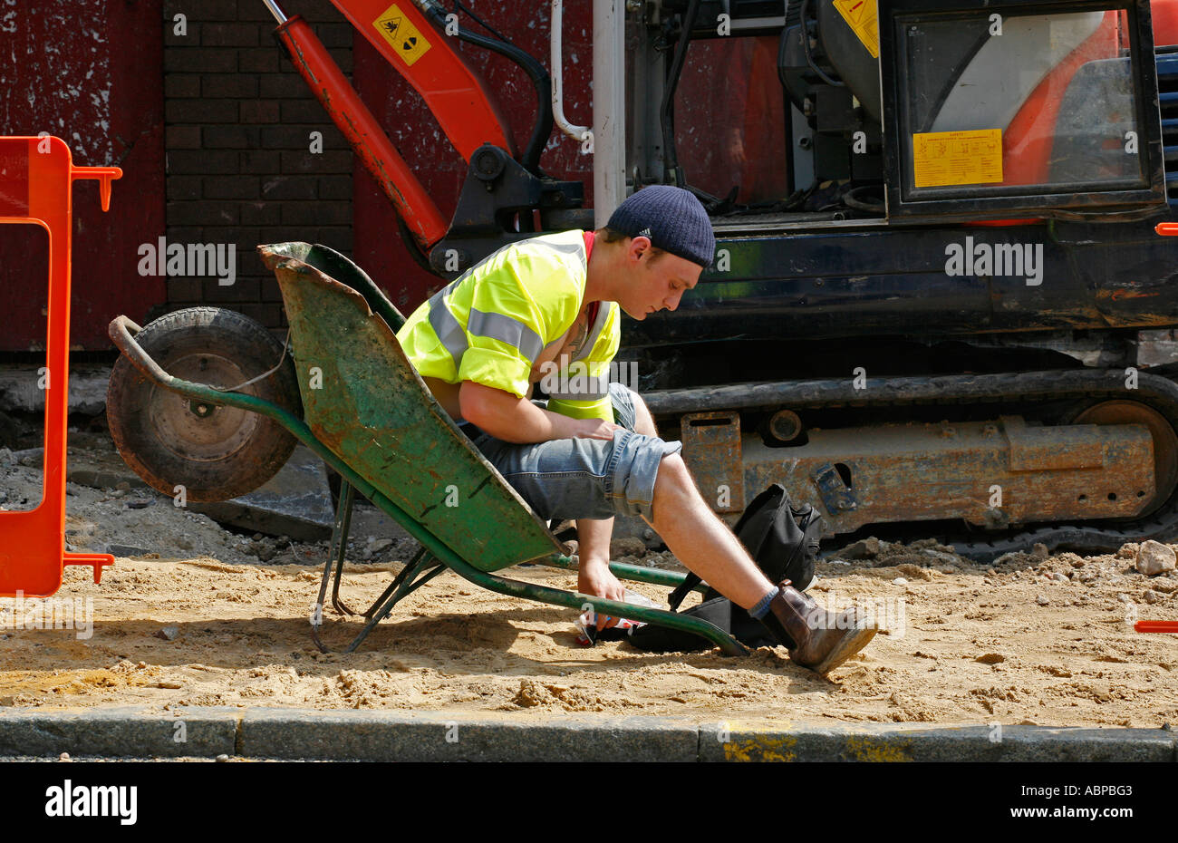 British lavoratore avente una pausa dal suo lavoro in appoggio una carriola per fumare una sigaretta. Foto Stock