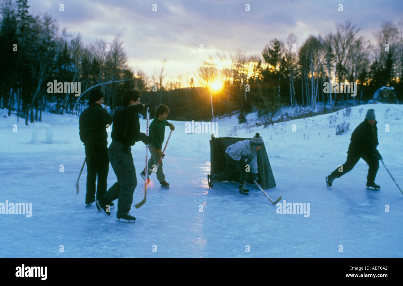 Ragazzi che giocano a hockey su un lago ghiacciato al tramonto Foto Stock