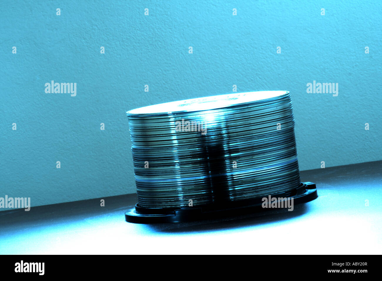 Una pila di lucidi compact disc su un perno in plastica sotto una luce blu soffusa, che illustrano i supporti di memorizzazione o l'archiviazione dei dati digitali. Foto Stock