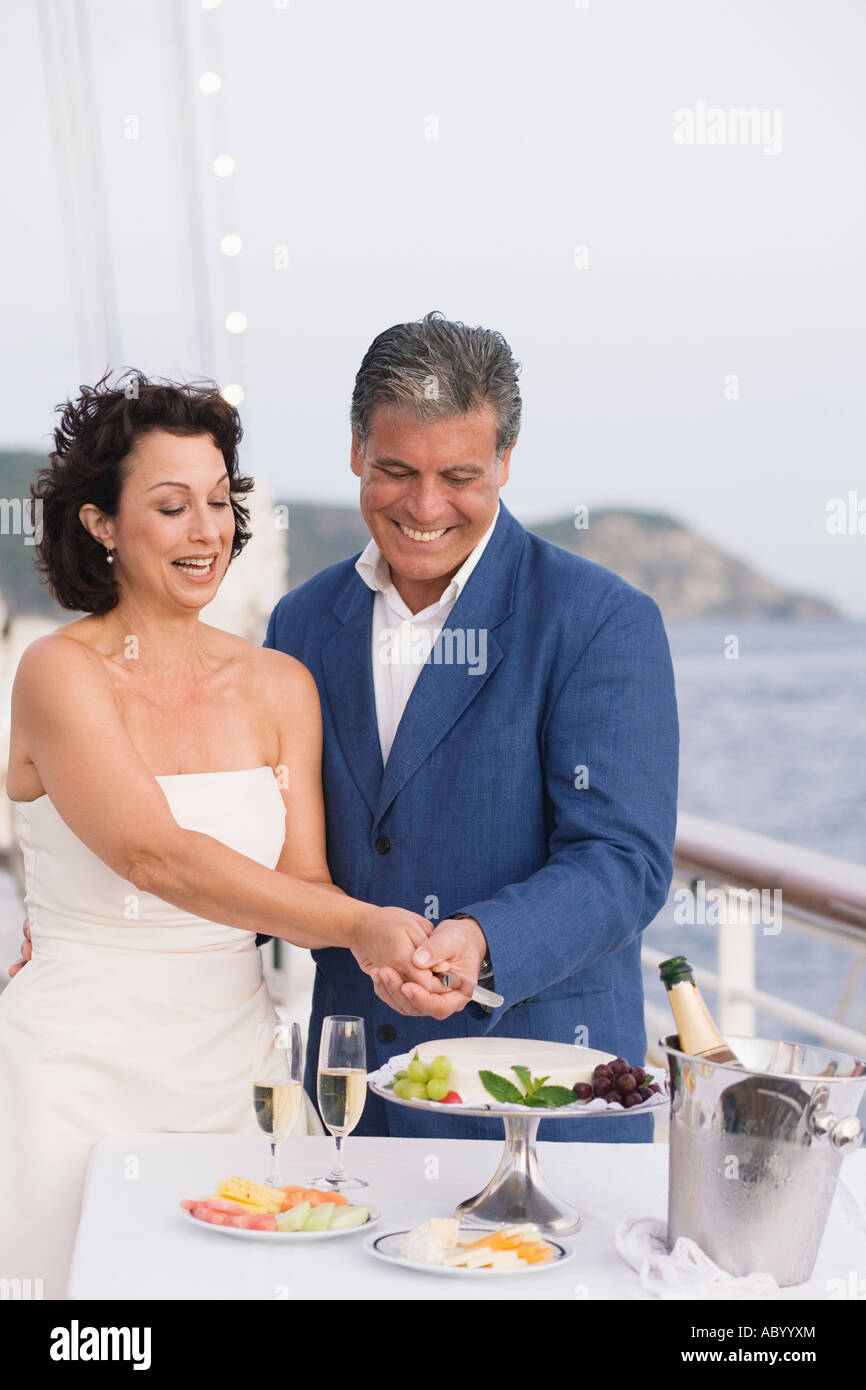 Sposa giovane il taglio di torta di nozze sulla coperta della barca Foto Stock