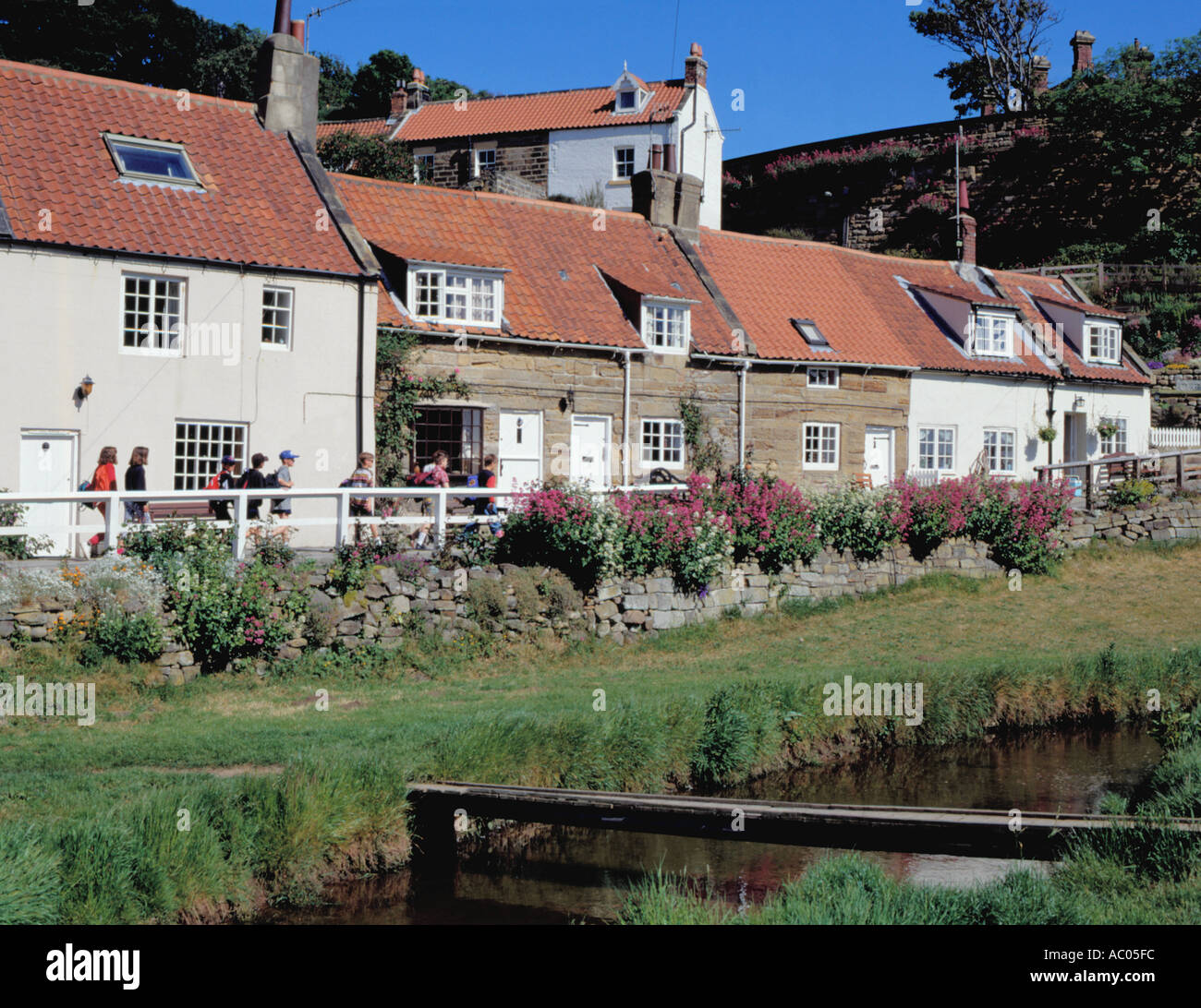 I giovani escursionisti passando pittoreschi cottage in pietra; Sandsend Village, vicino a Whitby, North Yorkshire, Inghilterra, Regno Unito. Foto Stock