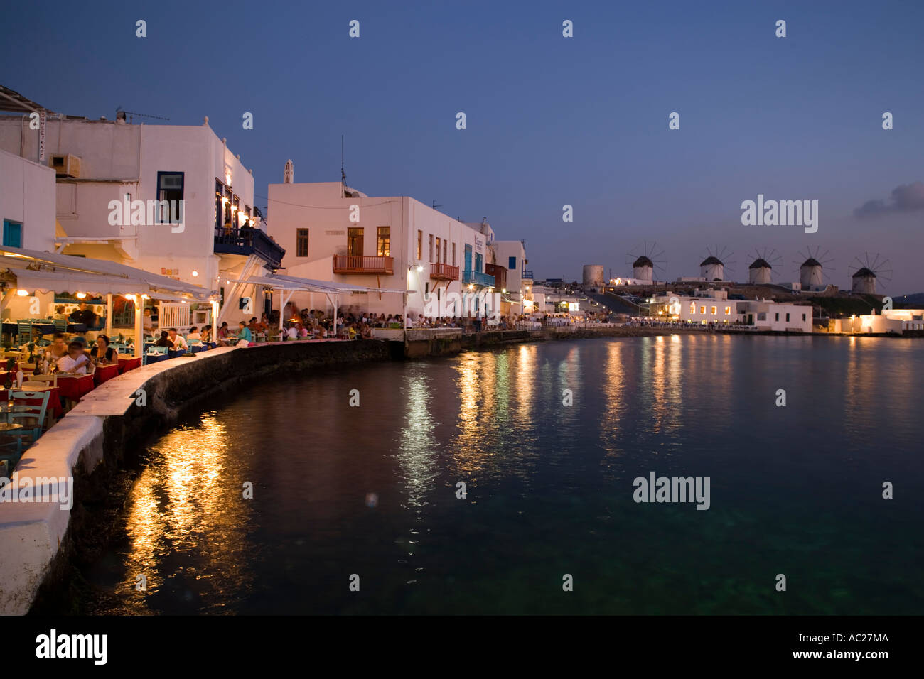 Vista lungo la banca con ristoranti e bar in serata windmilles in background la piccola Venezia città di Mykonos Mykonos Grecia Foto Stock