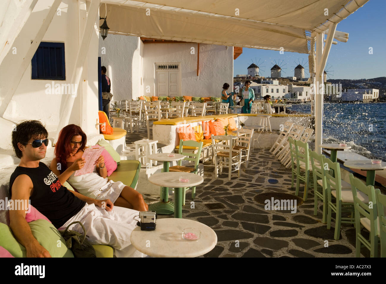 La gente seduta nel ristorante direttamente in mare di mulini a vento in background la piccola Venezia città di Mykonos Mykonos Grecia Foto Stock