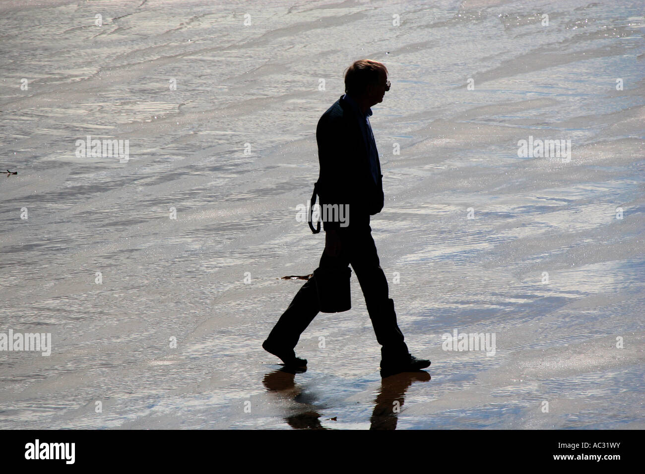 Silhouette di uomo a camminare lungo una spiaggia bagnata. Foto Stock