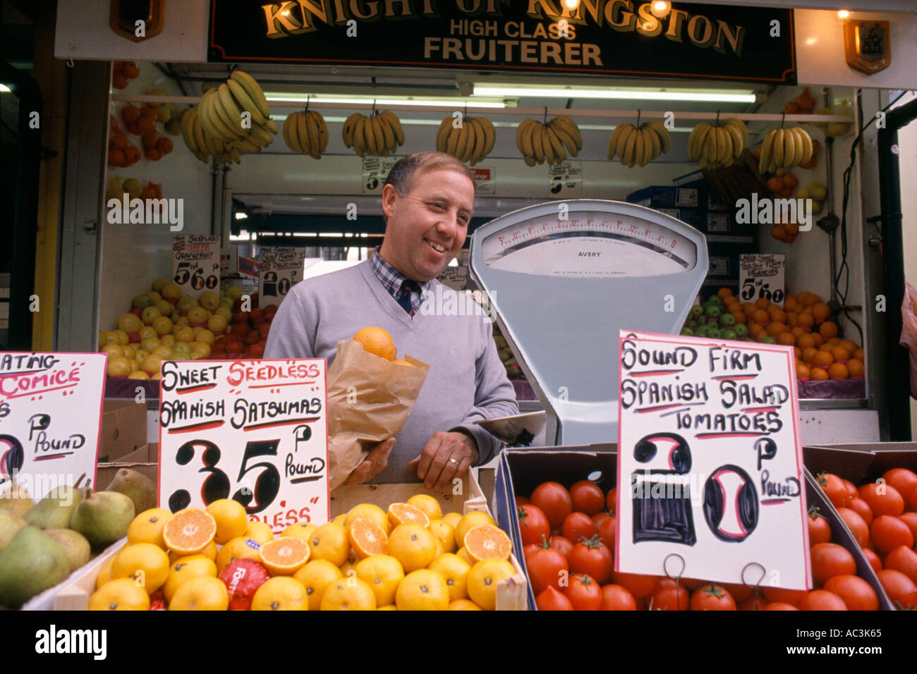 Fruttivendolo per la vendita di frutta e verdura per il suo negozio di stallo a Kingston upon Thames Inghilterra Foto Stock