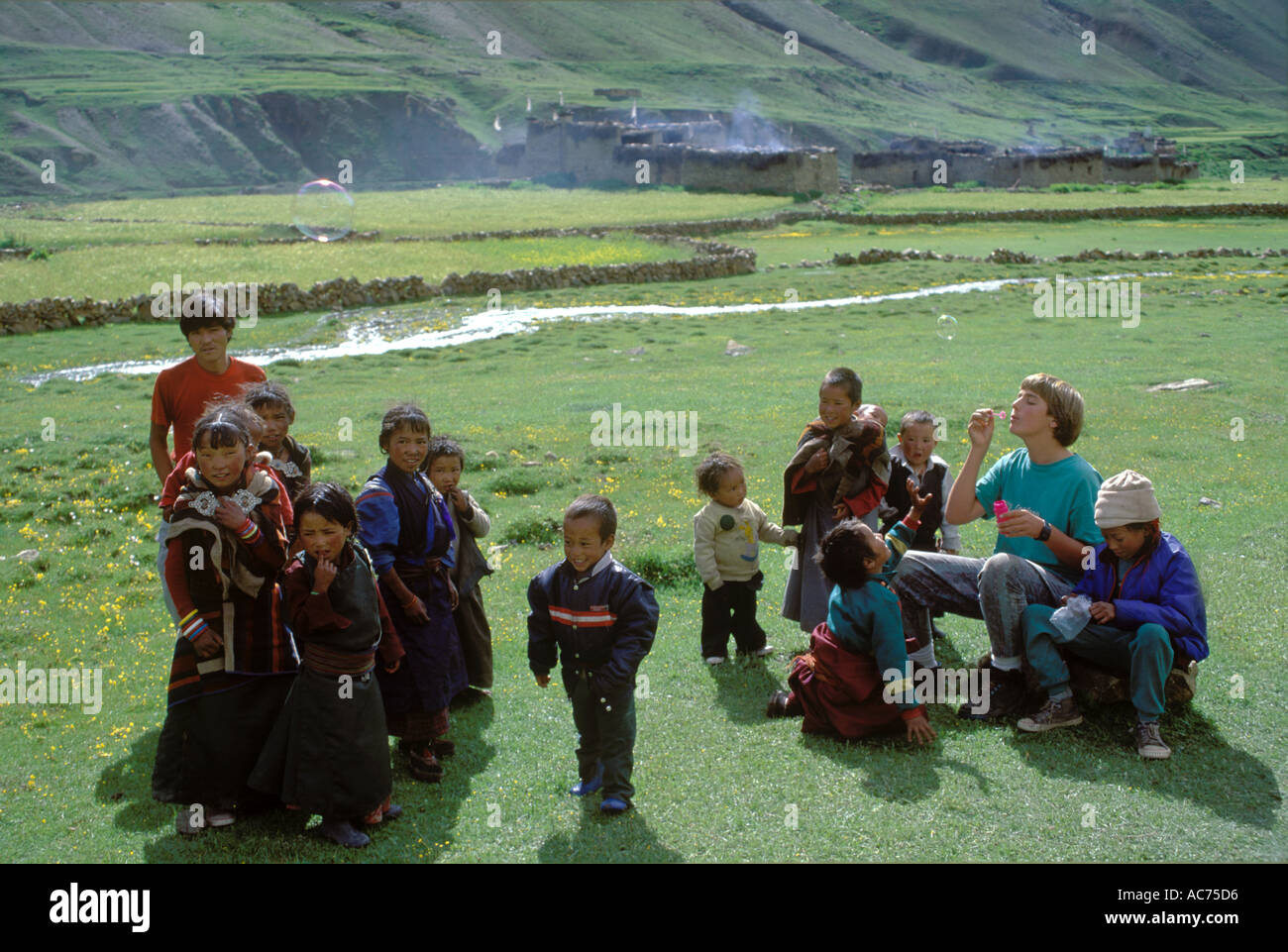 Un turista boAA TOURIST BODHI soffia bolle per bambini nepalesi in campi di orzo di DO TARAP VALLEY DOLPO NEPALdhi si brucia Foto Stock