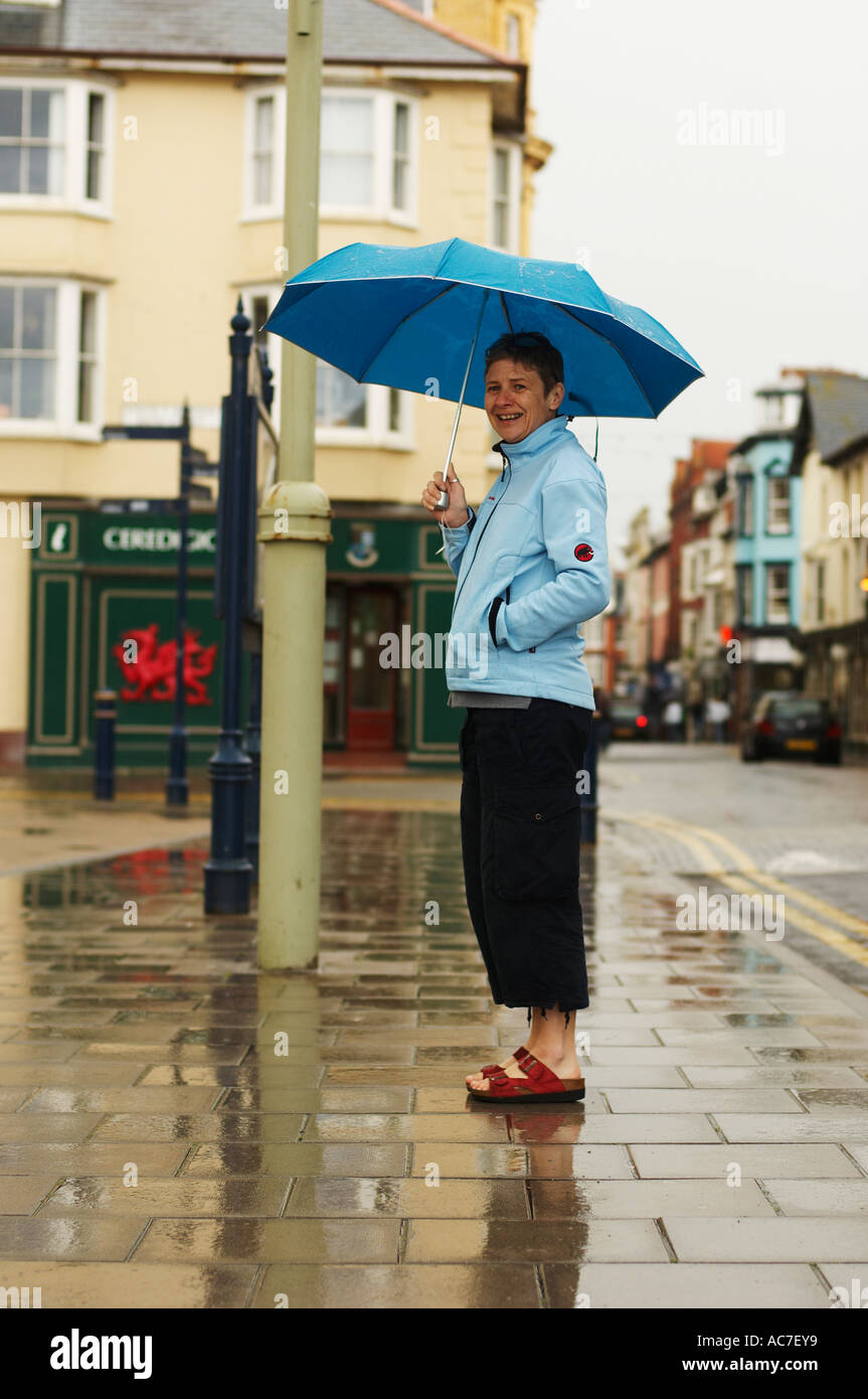 40 qualcosa di donna che indossa sandali in piedi sotto un ombrello blu sotto la pioggia Aberystwyth Wales UK Foto Stock